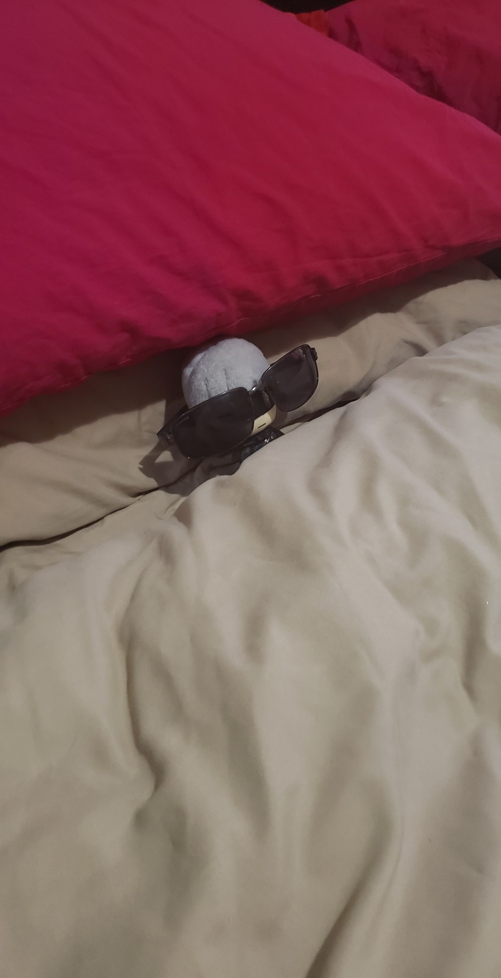 A plush of the character 9S from the game NieR: Automata wearing sunglasses while laying down in a bed way too big for him.