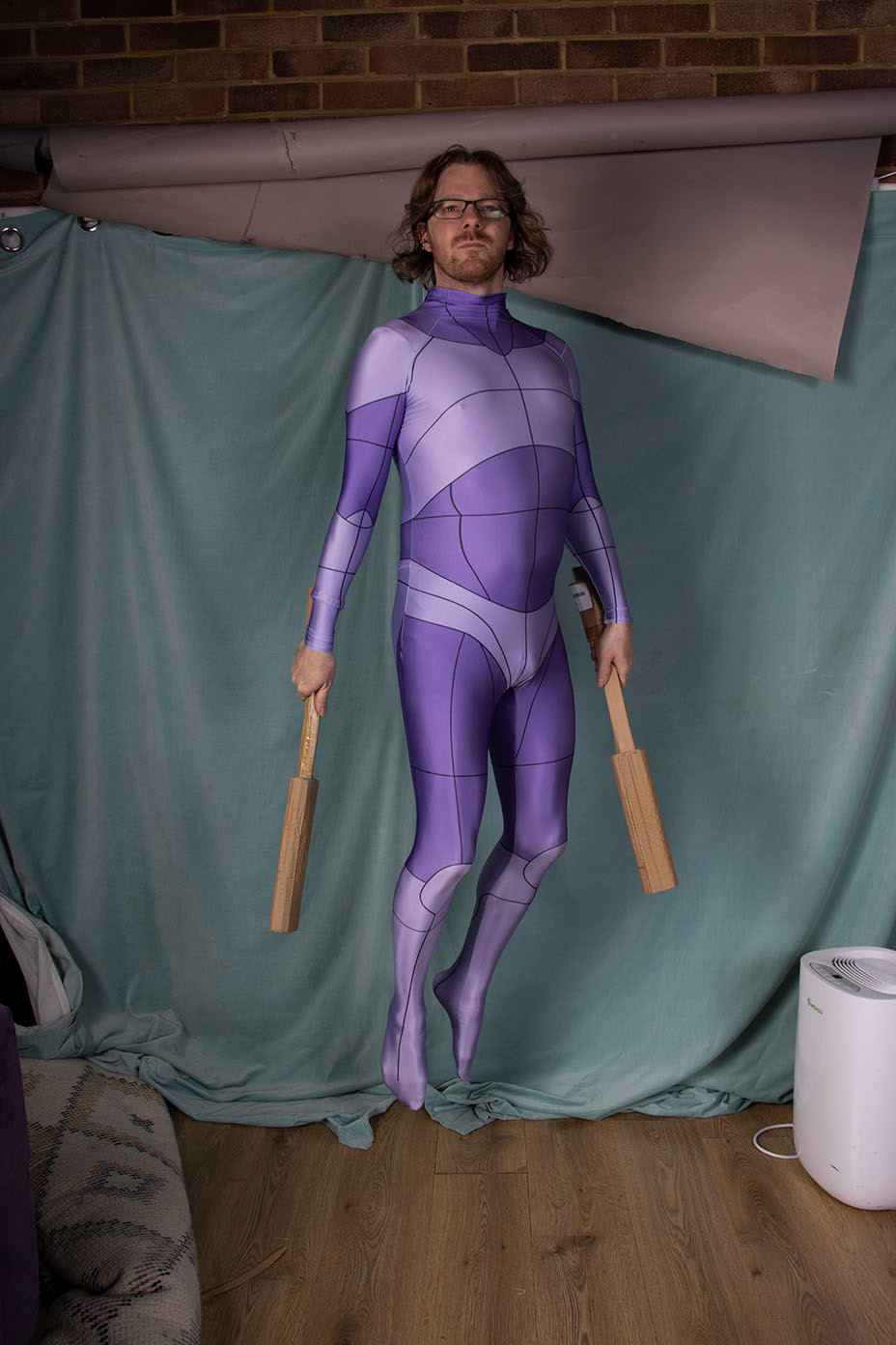 A man wearing a purple body suit with isolated body parts drawn on it, jumping into the air.