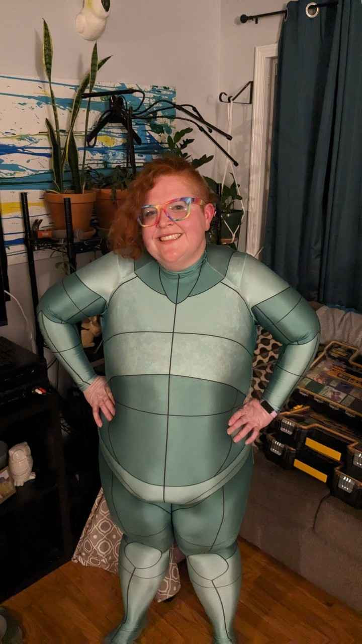 A woman with her hands on her hips in a green body suit with isolated body parts drawn on it.