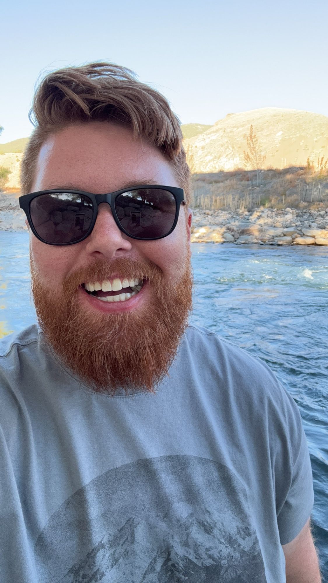 Ginger cub smiling with mouth open in front of a river.