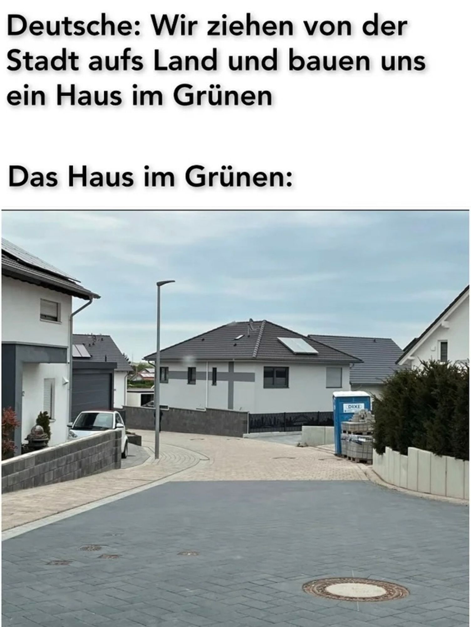 Deutsche: wir ziehen von der Stadt aufs Land und bauen uns ein Haus im Grünen. Das Haus im Grünen:
Foto von Einfamilienhäusern, komplett versiegelt, eng stehend, kein Grün