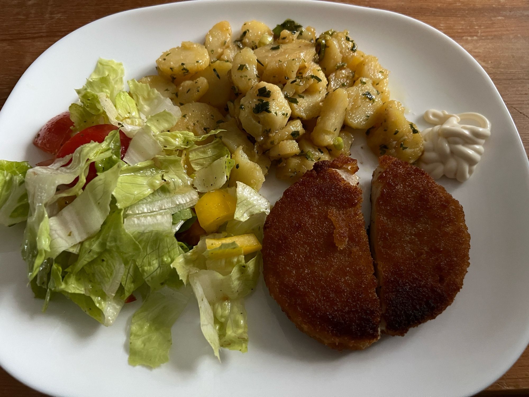 Weißer Teller mit Hähnchenschnitzel, selbstgemachtem Kartoffelsalat und gemischtem Salat.