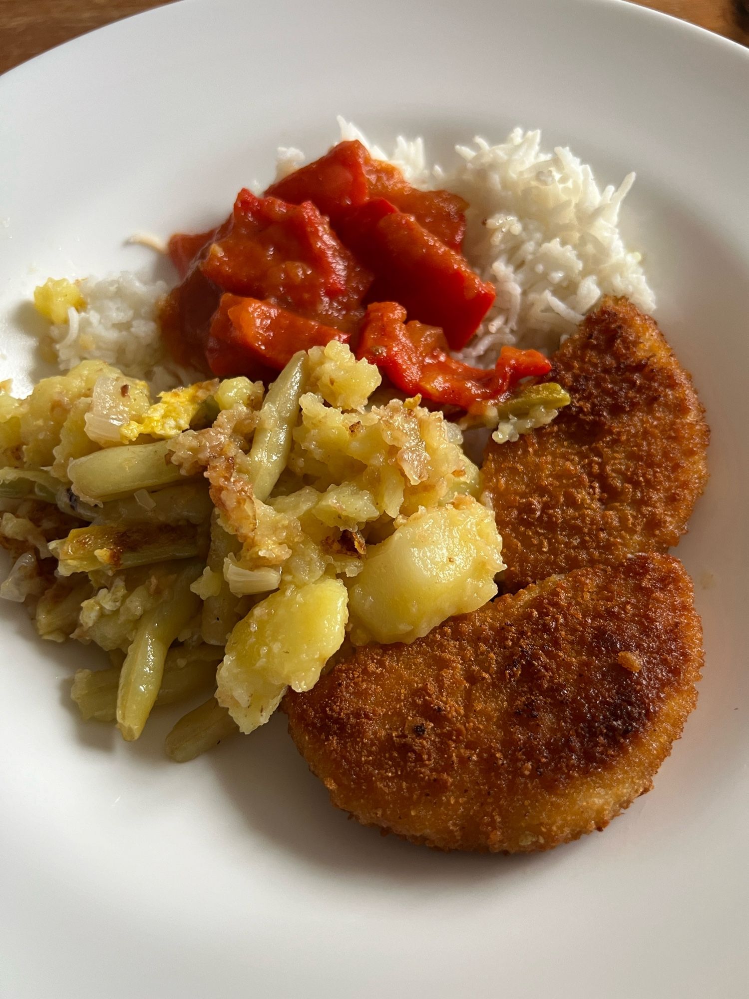 Weißer Teller mit Hühnerschnitzel, Reis, Reste von Kartoffeln und Bohnen und Paprikasauce.