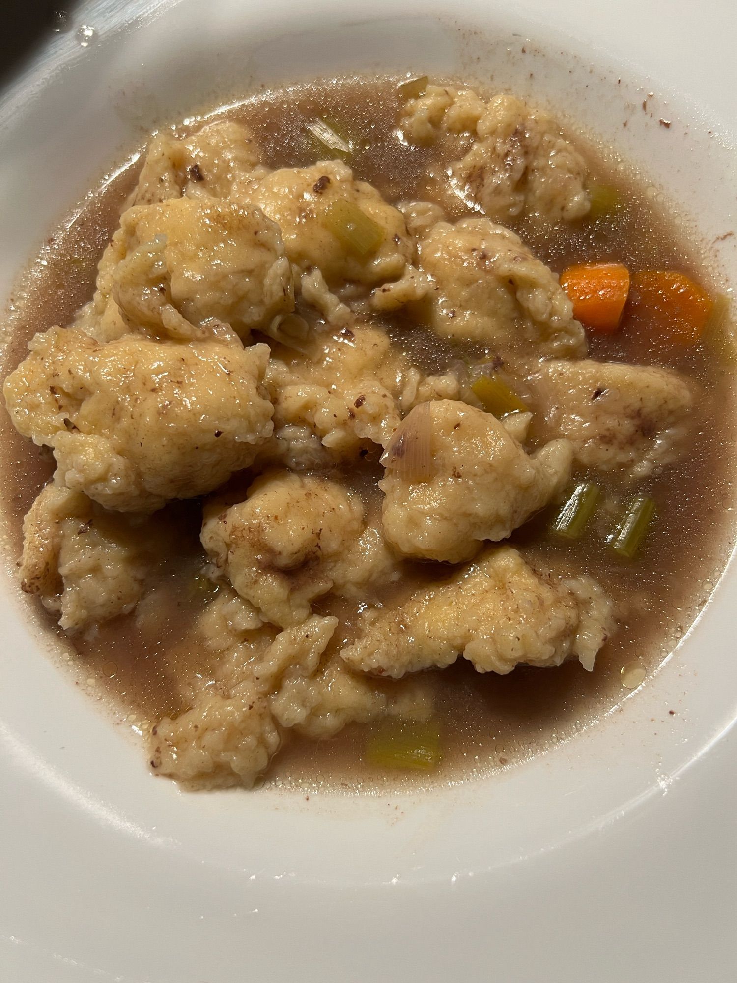 Weißer Teller mit Rindfleischsuppe mit Gemüse und Mehlklößchen.