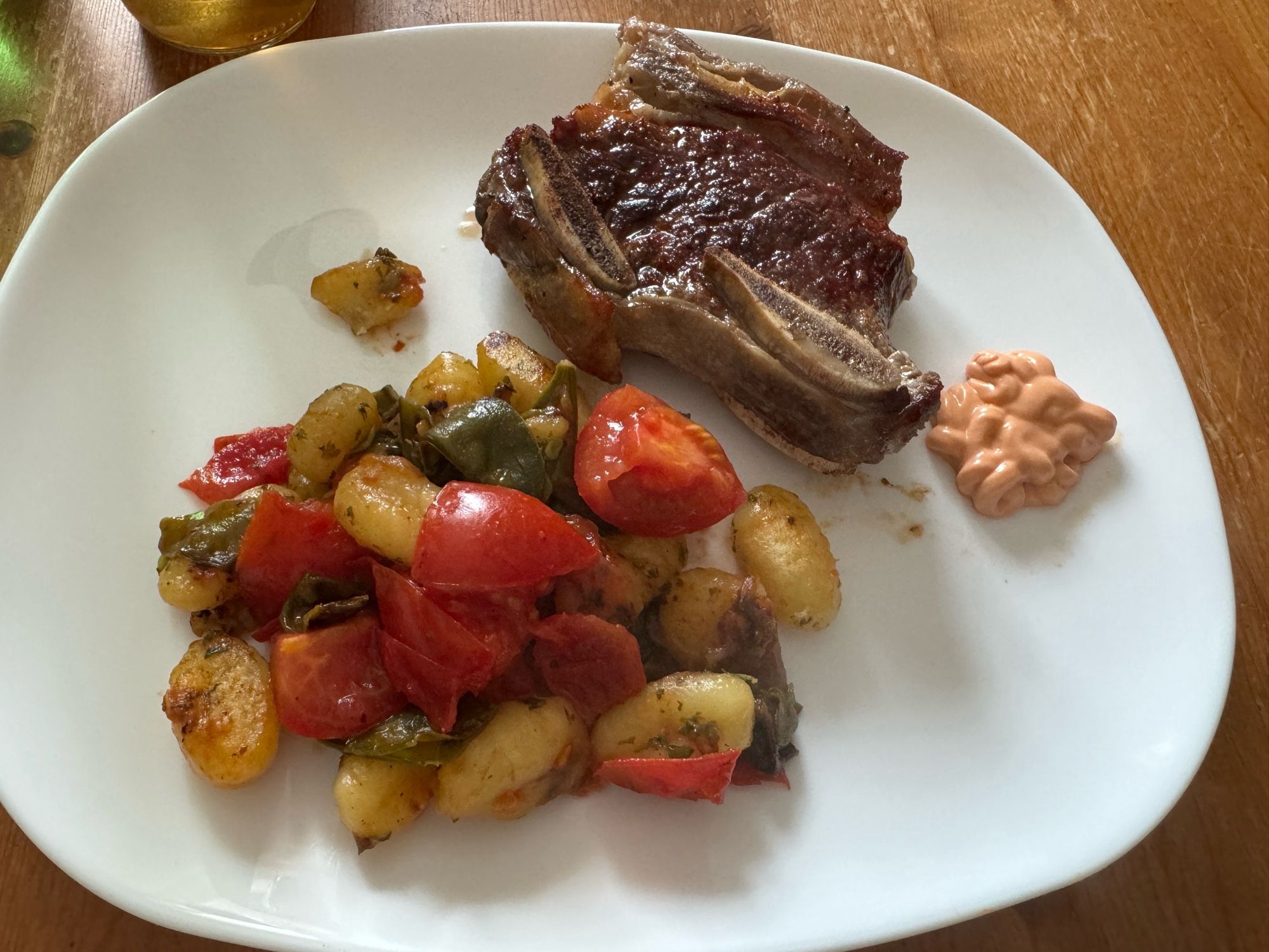 Weißer Teller mit einem Stück Short Rib mit Gemüse-Gnocchi-Pfanne mit Tomaten.