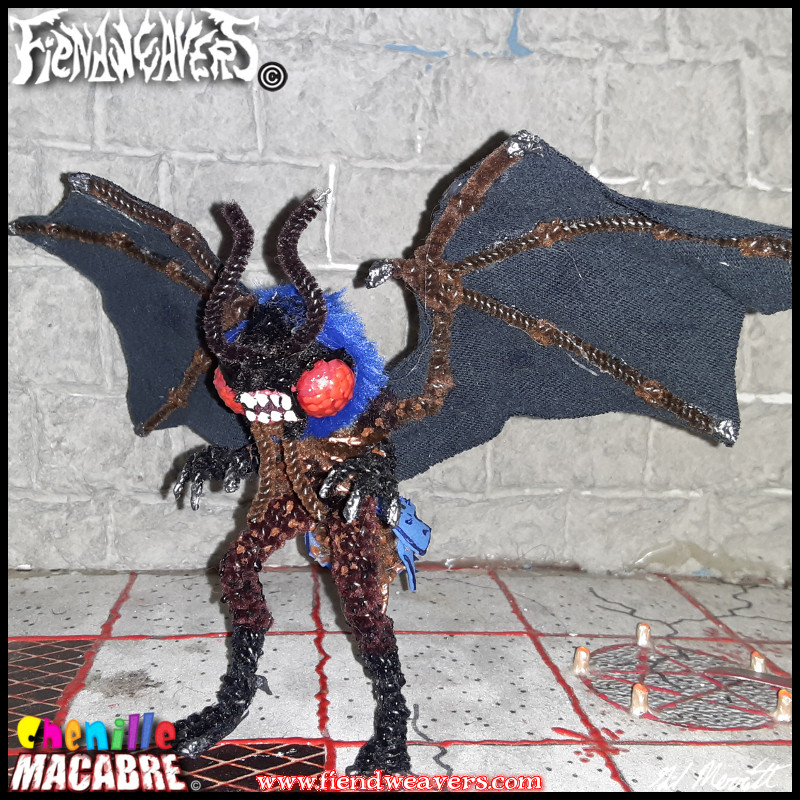 A pipe cleaner figure I built of the Mothman. It has a brown body, huge red eyes with a toothy mouth between, black bat wings, and blue plume. Stands 3" (7.62 cm) high.