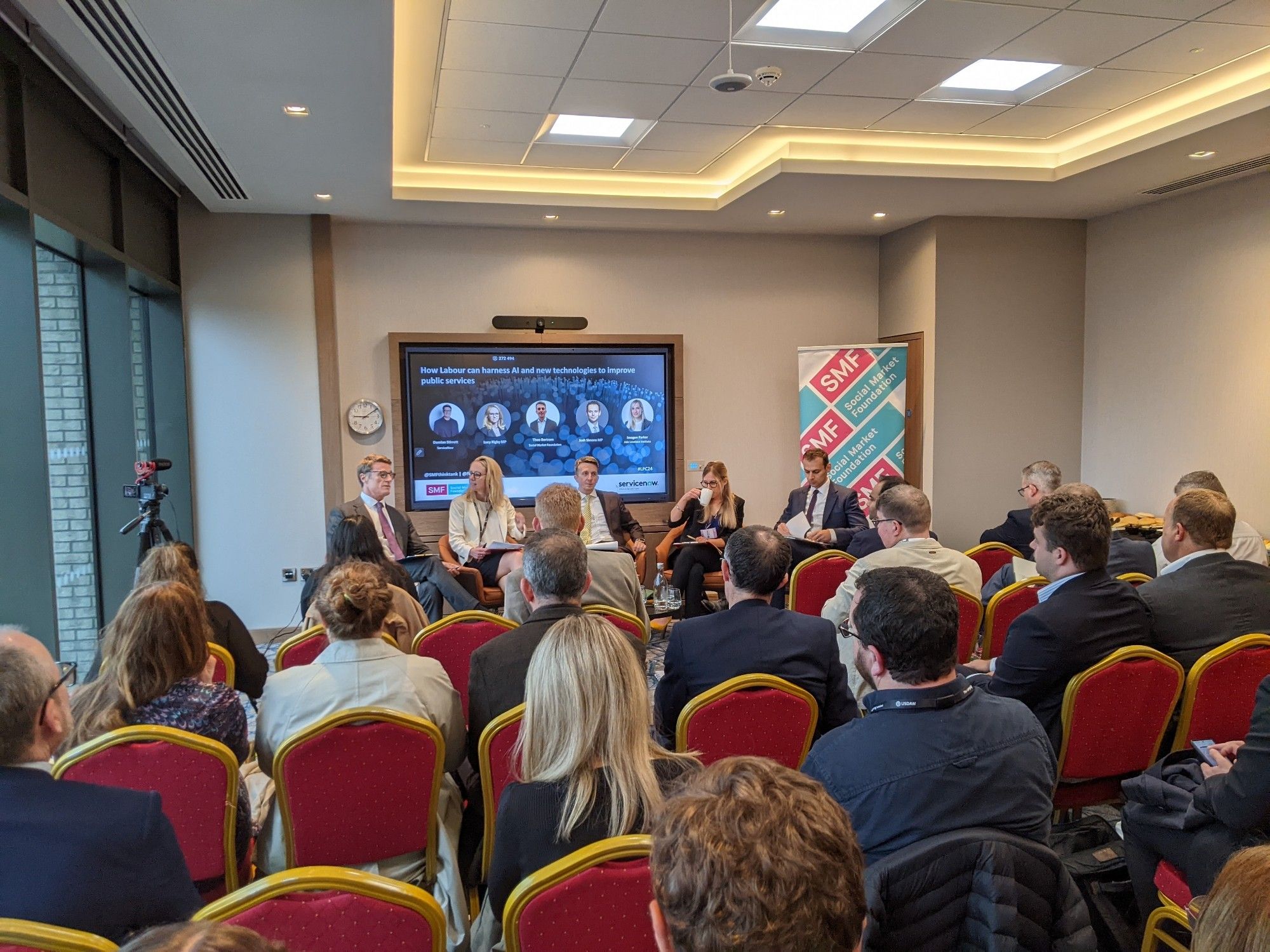 Damian Stirrett of ServiceNow, Lucy Rigby MP, Theo Bertram of SMF, Imogen Parker of the Ada Lovelace Institute and Josh Simons MP sit in front of a slide with event details and an SMF banner