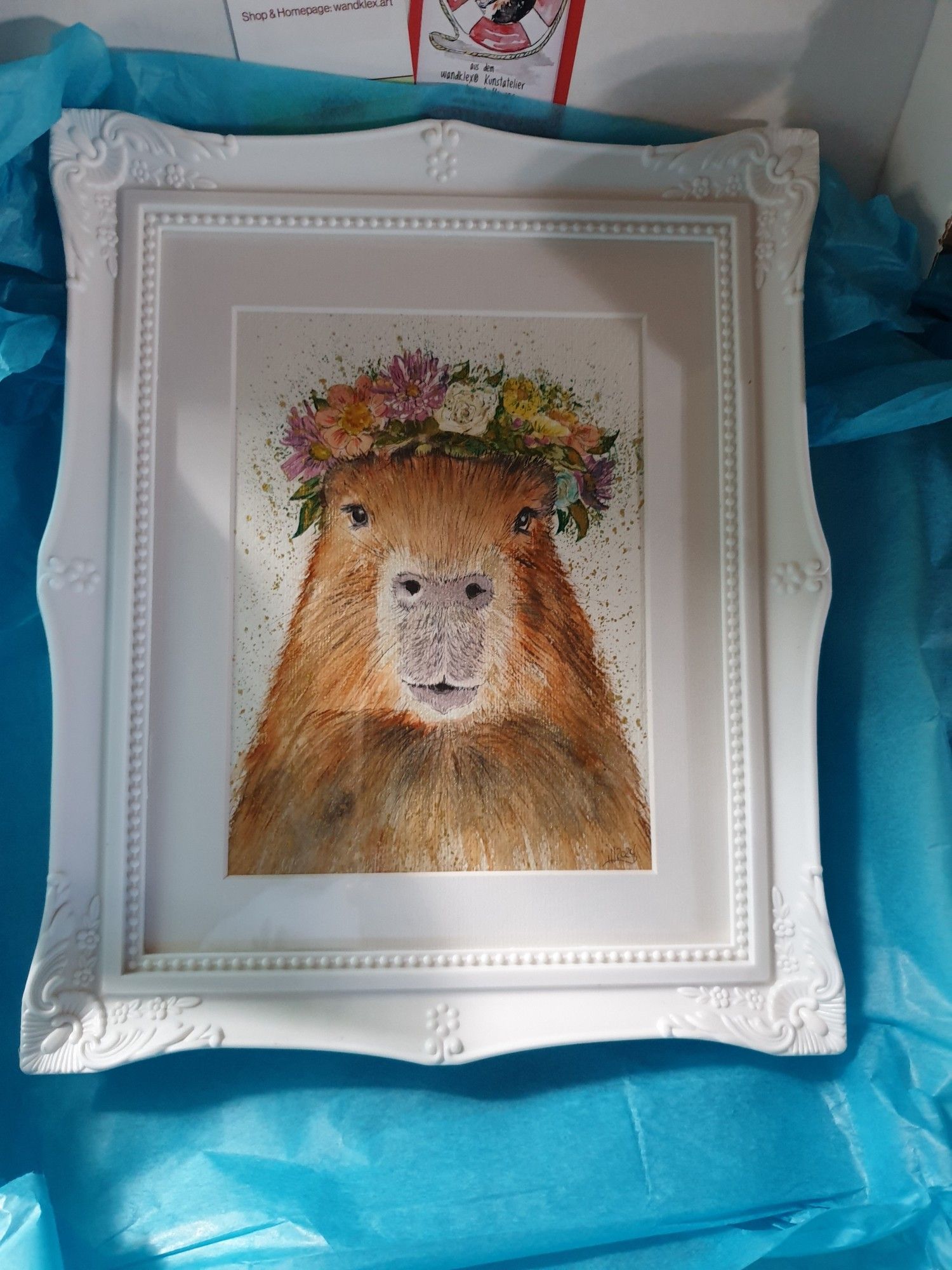 Aquarell eines Capybaras mit Blumenkranz auf dem Kopf.