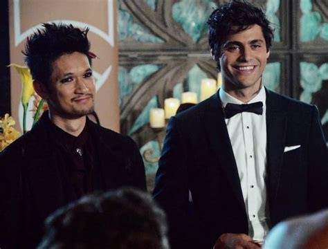 Magnus and Alec at their wedding reception. They stand next to each other, both smiling.