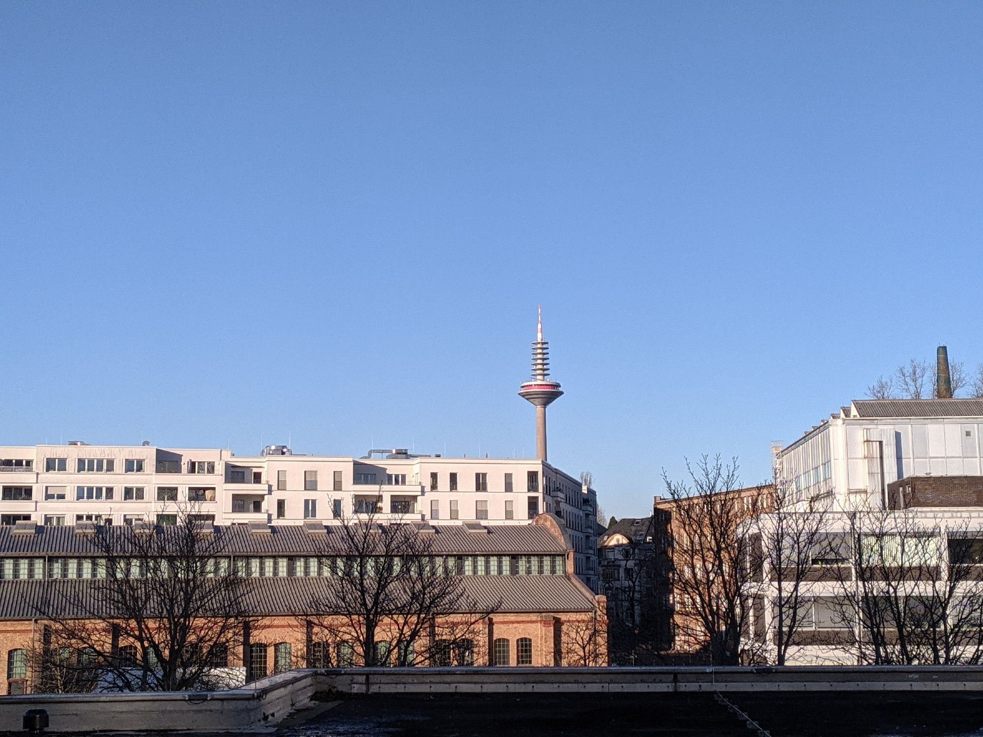 Der Ginnheimer Spargel über dem Bockneheimer Depot und einem großen Wohnhaus, aus dessen Ecke er hervorzuragen scheint. Die Dondorf-Druckerei daneben, ein kürzlich besetztes Haus, sowie die Gebäude der Universitätsbibliothek J.C. Senckenberg