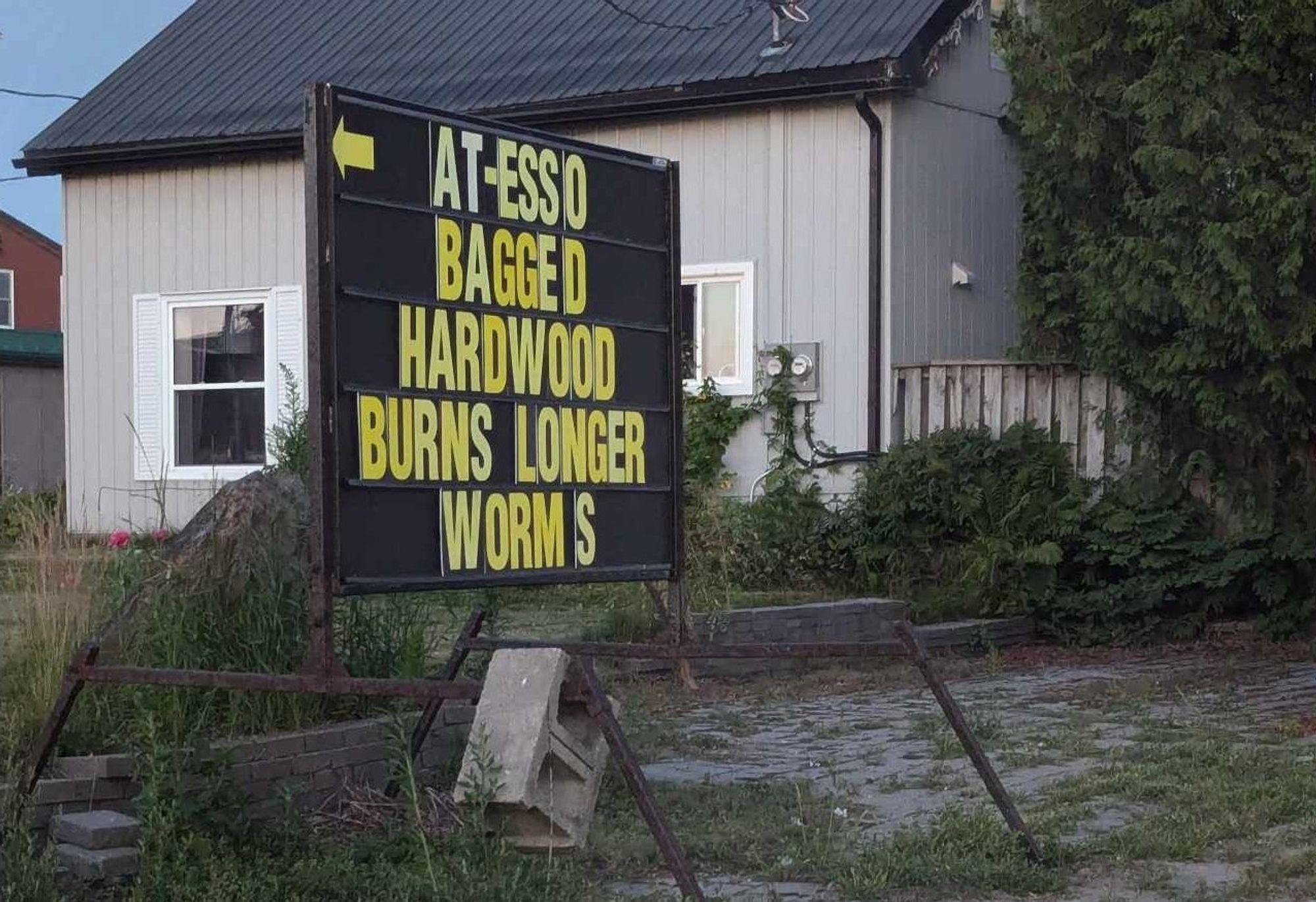 A sign that reads "at-esso bagged hardwood burns longer worms" where each word, except "burns longer", is on its own line