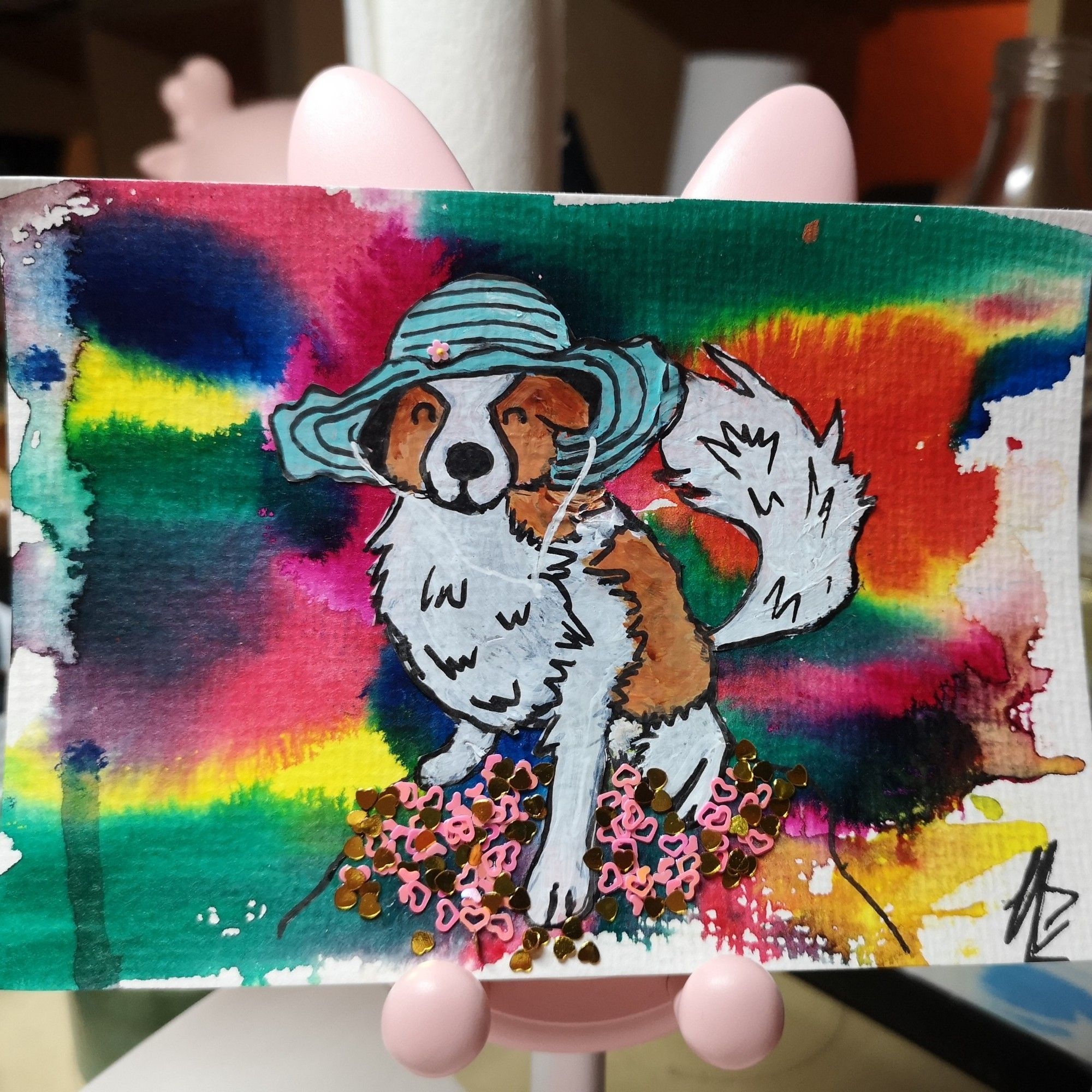 Eine kunterbunte mit Acryl bemalte Postkarte mit einem kleinen weiß-braunen Hund mit türkisem Hut im Zentrum.