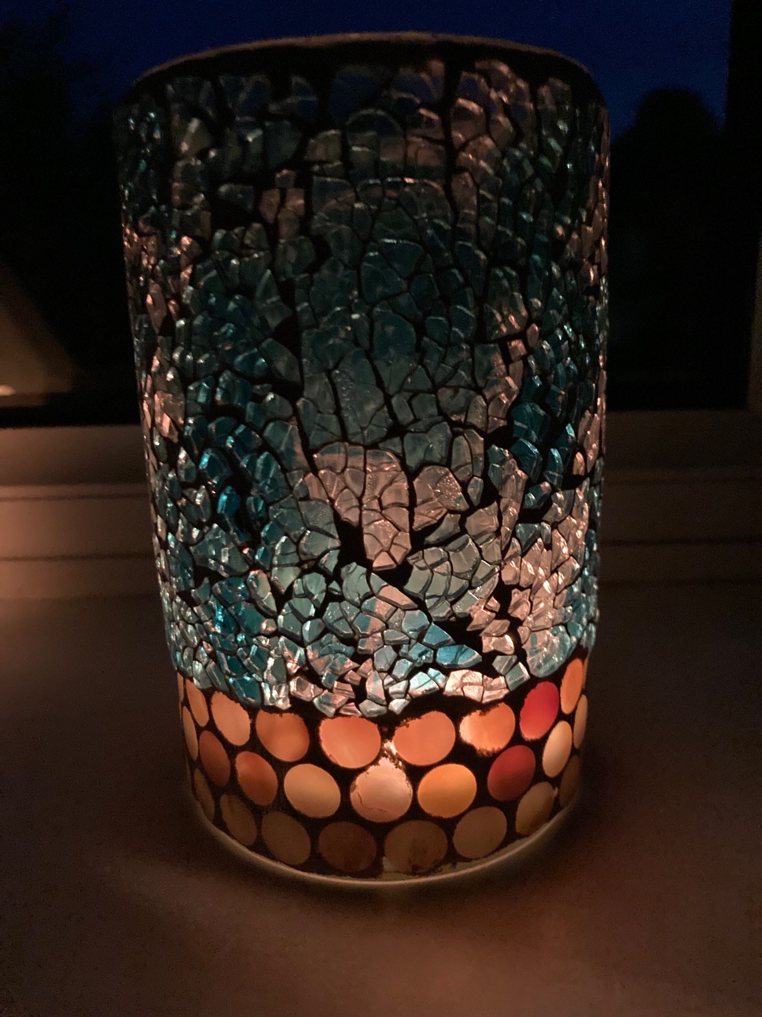 The light of a candle shining through a translucent blue and clear glass candle holder.