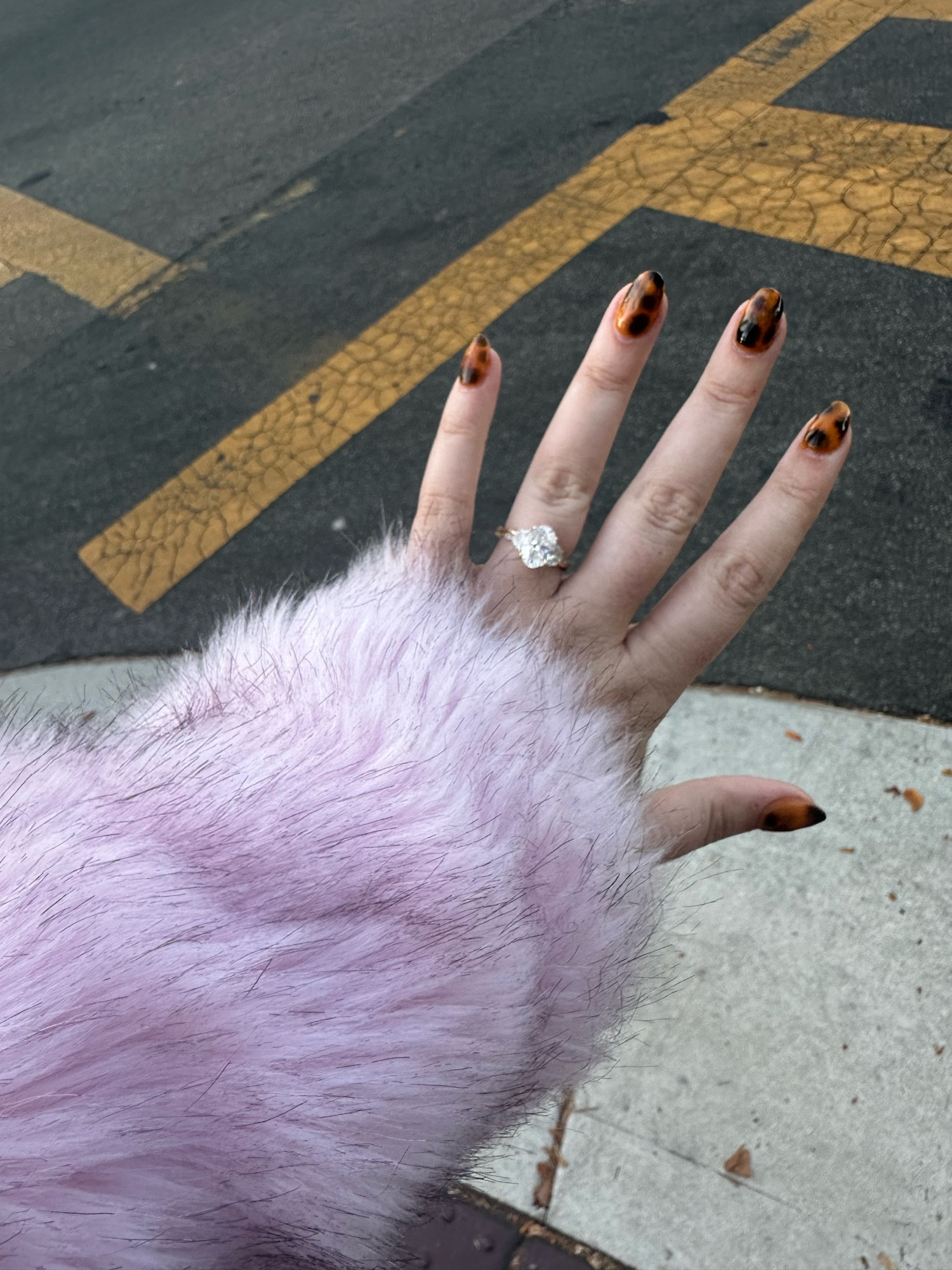 A left hand with a pink fur sleeve. Nails are a first attempt at a tortoiseshell pattern. short-medium length almond shape