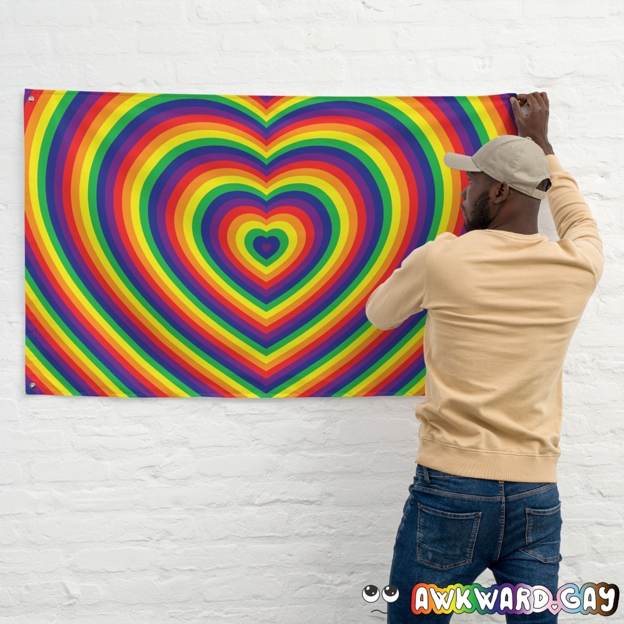 Mockup of a person hanging a flag on a white wall. The flag features conctentric hearts in rainbow pride colours