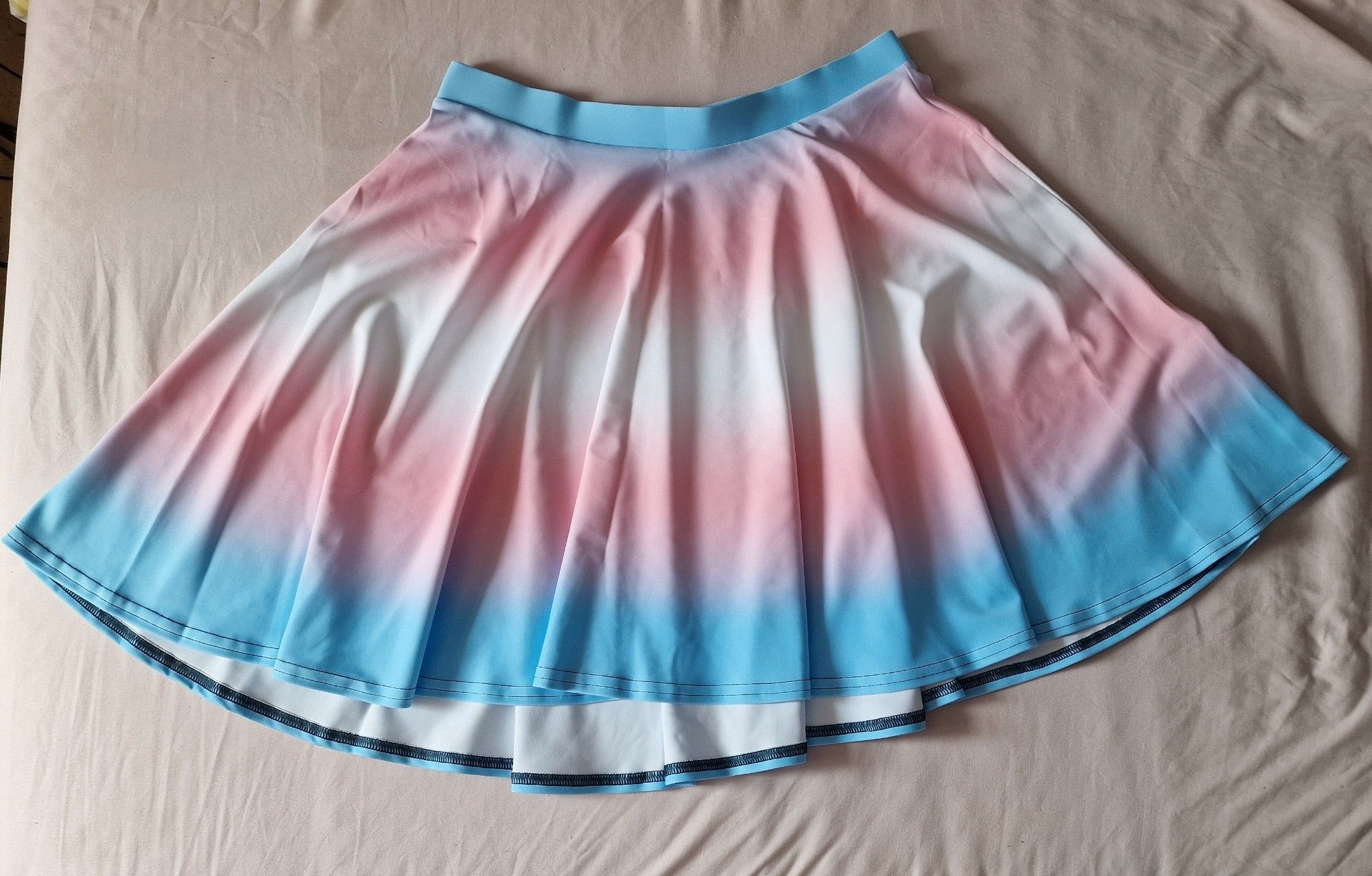 A skater skirt with a trans pride flag gradient print, spread out on a bed