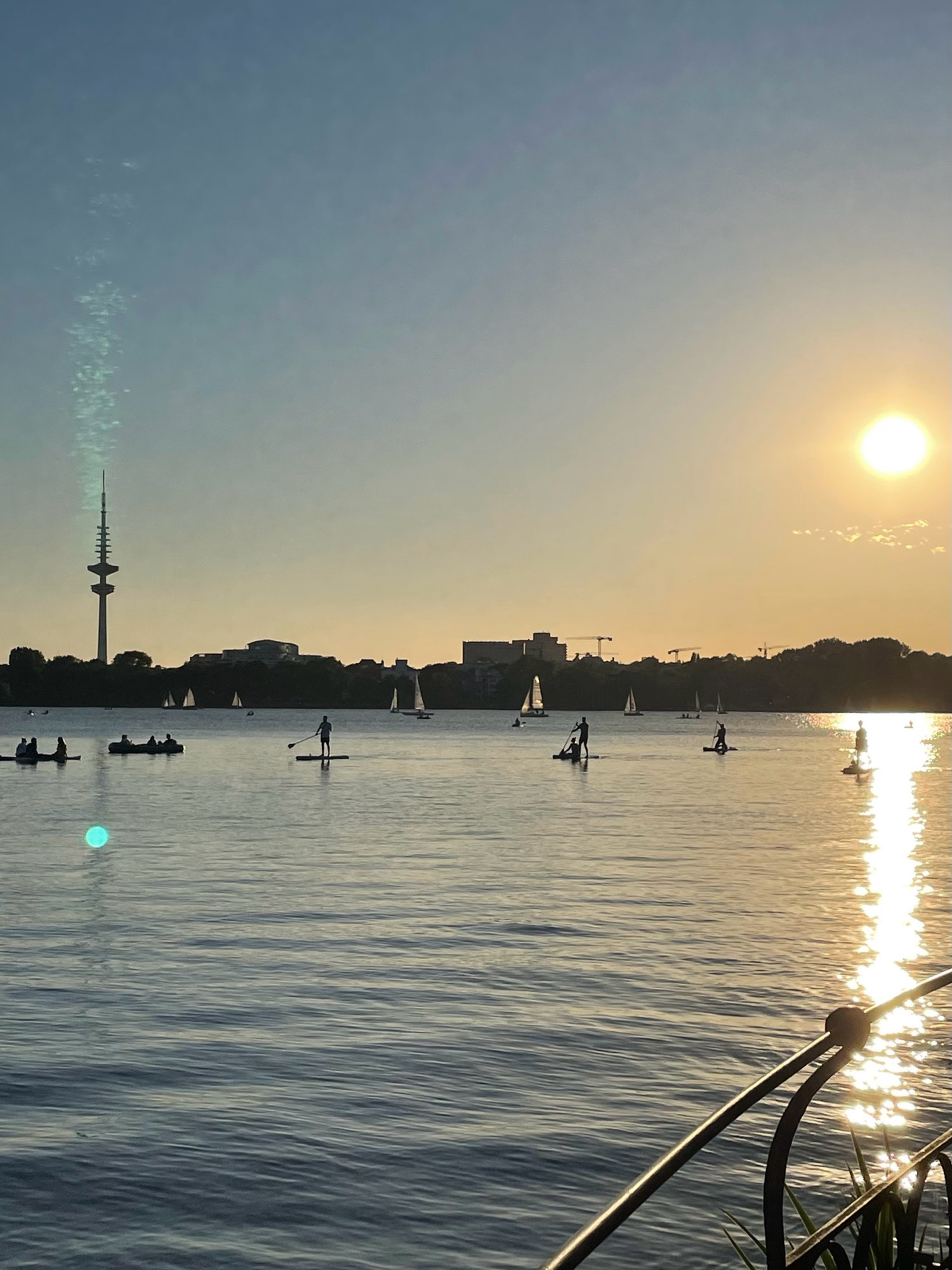 Blick auf die Aussenalster bei Sonnenuntergang. Auf der Alster Bötchen und Paddler. Am Horizont der Messeturm.