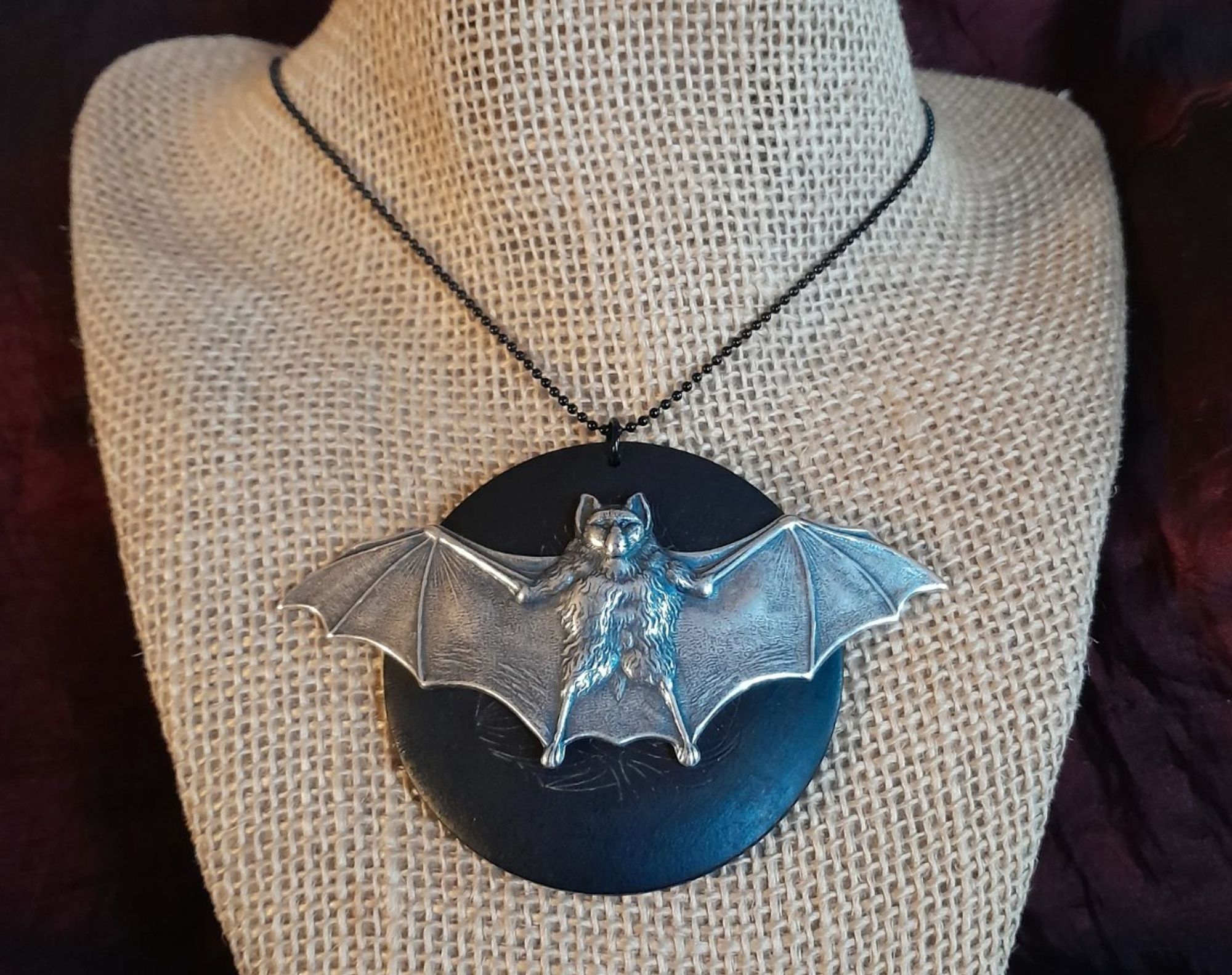 Big bold silver-tone bat, wide-winged, on a blackened wooden medallion with etching on a 24 inch black ball-joint chain, approximately 5 x 5 inches