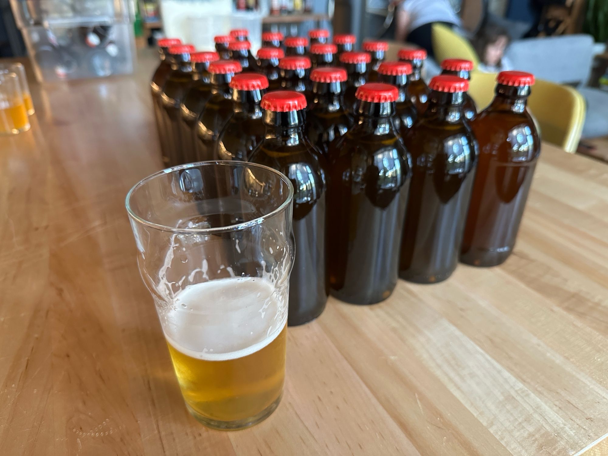 25 bottles of homebrew pale ale, with some beer in a pint glass in the foreground