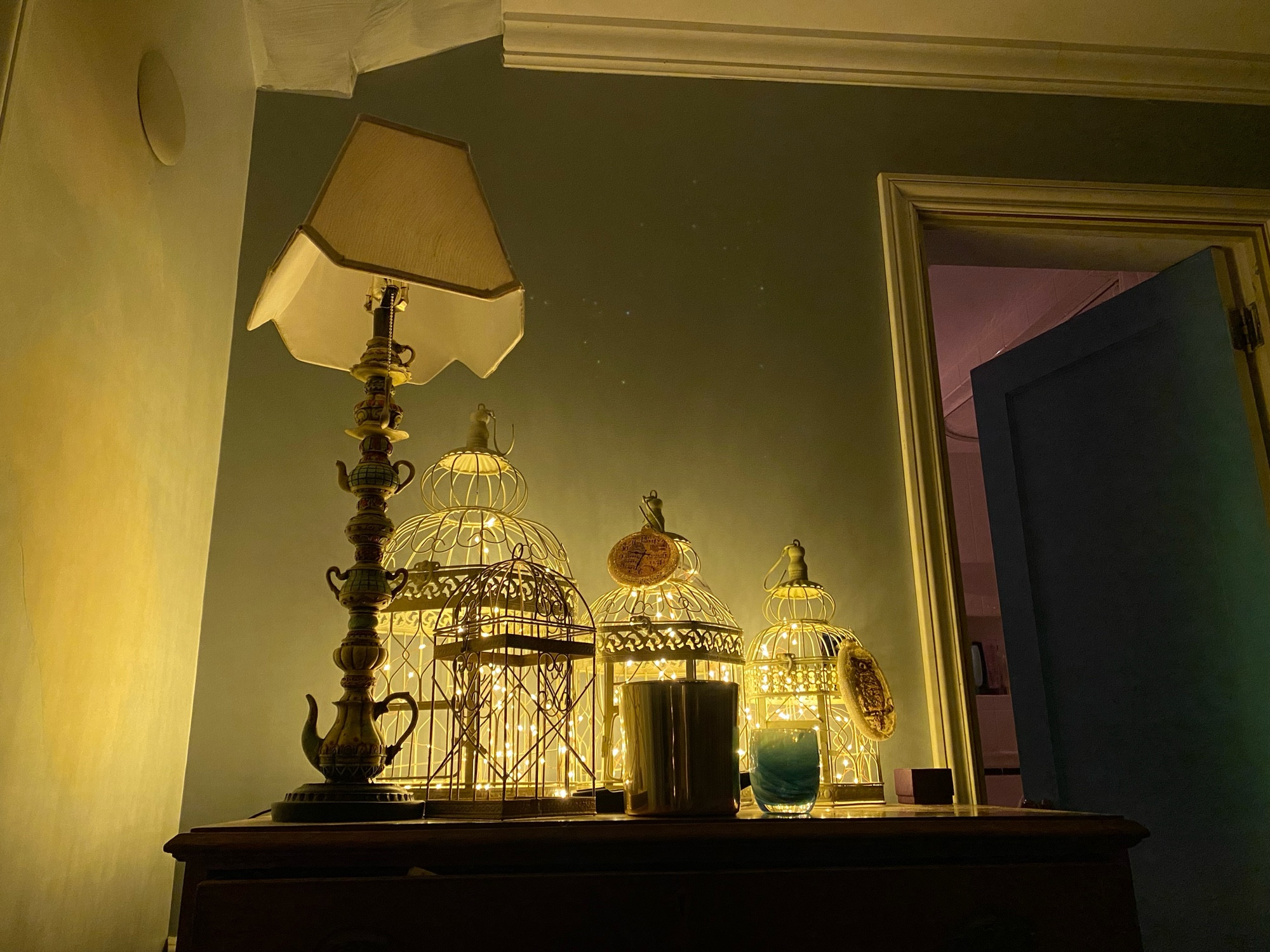 A picture of my dresser with three birdcages with fairy lights in them, also my teapot lamp and candle holders.