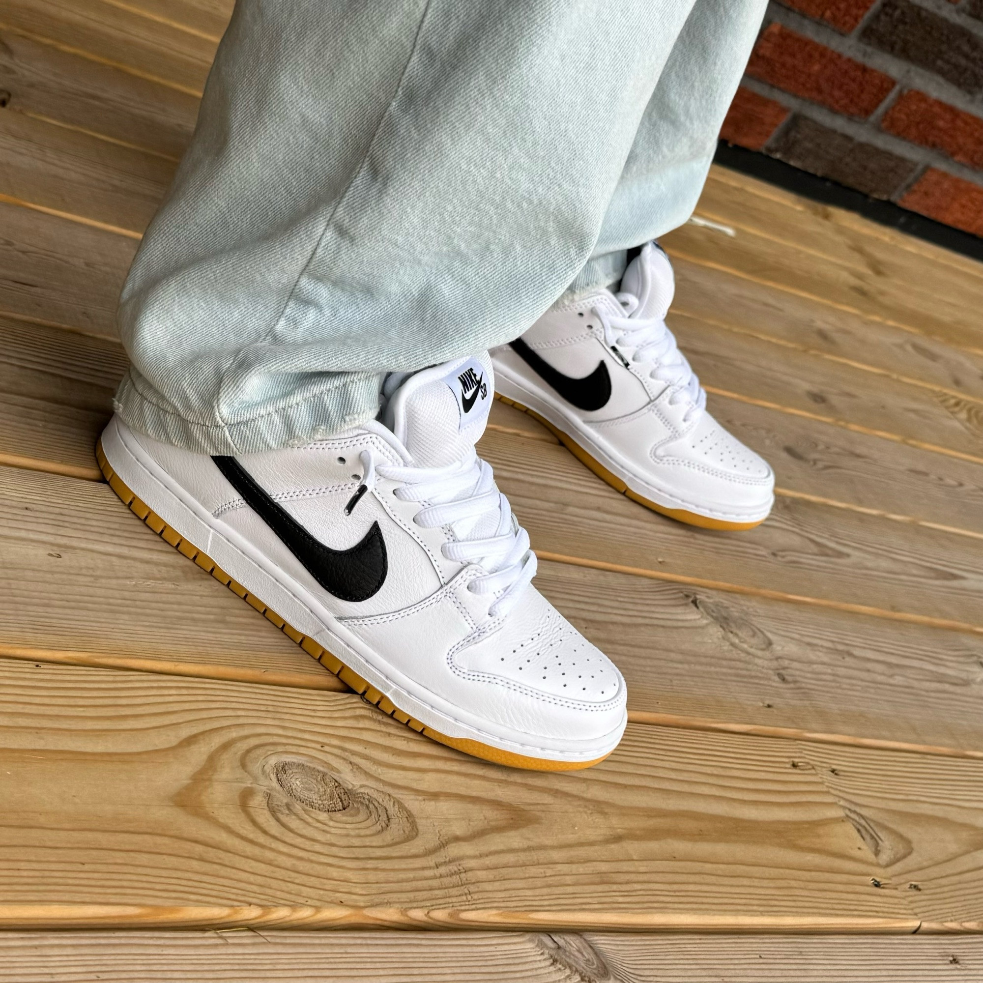 A pair of white Nike dunks with a black swoosh and gum soles