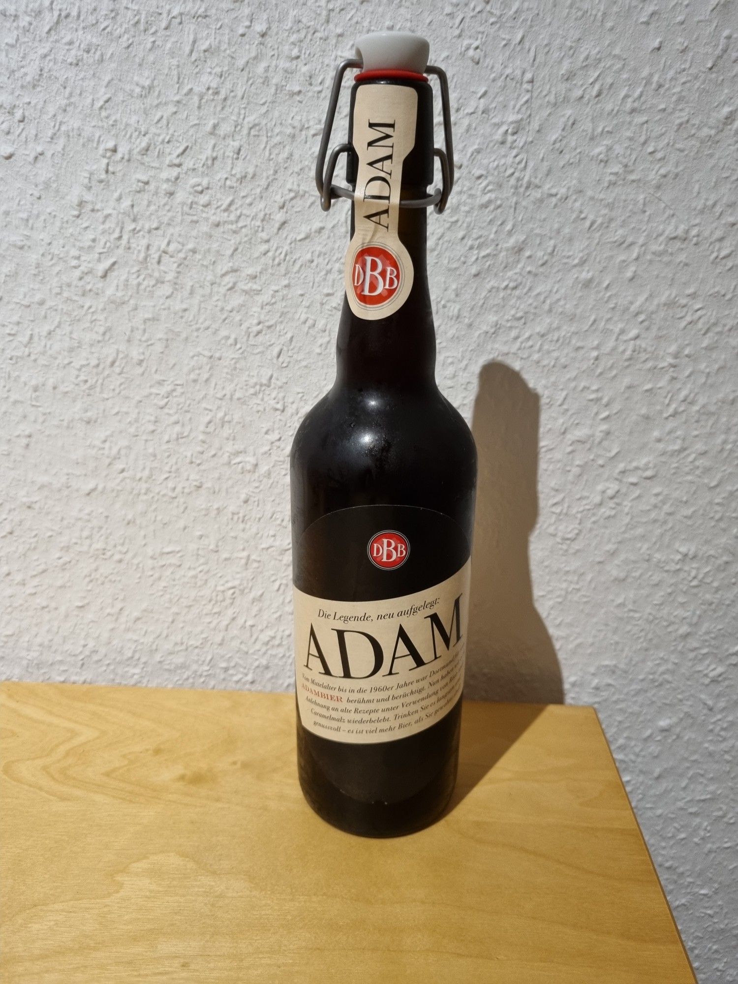 Ein geschlossene Bügelflasche Adam-Bier der dortmunder Bergmann Brauerei auf Holztisch vor weißer Raufasertapete