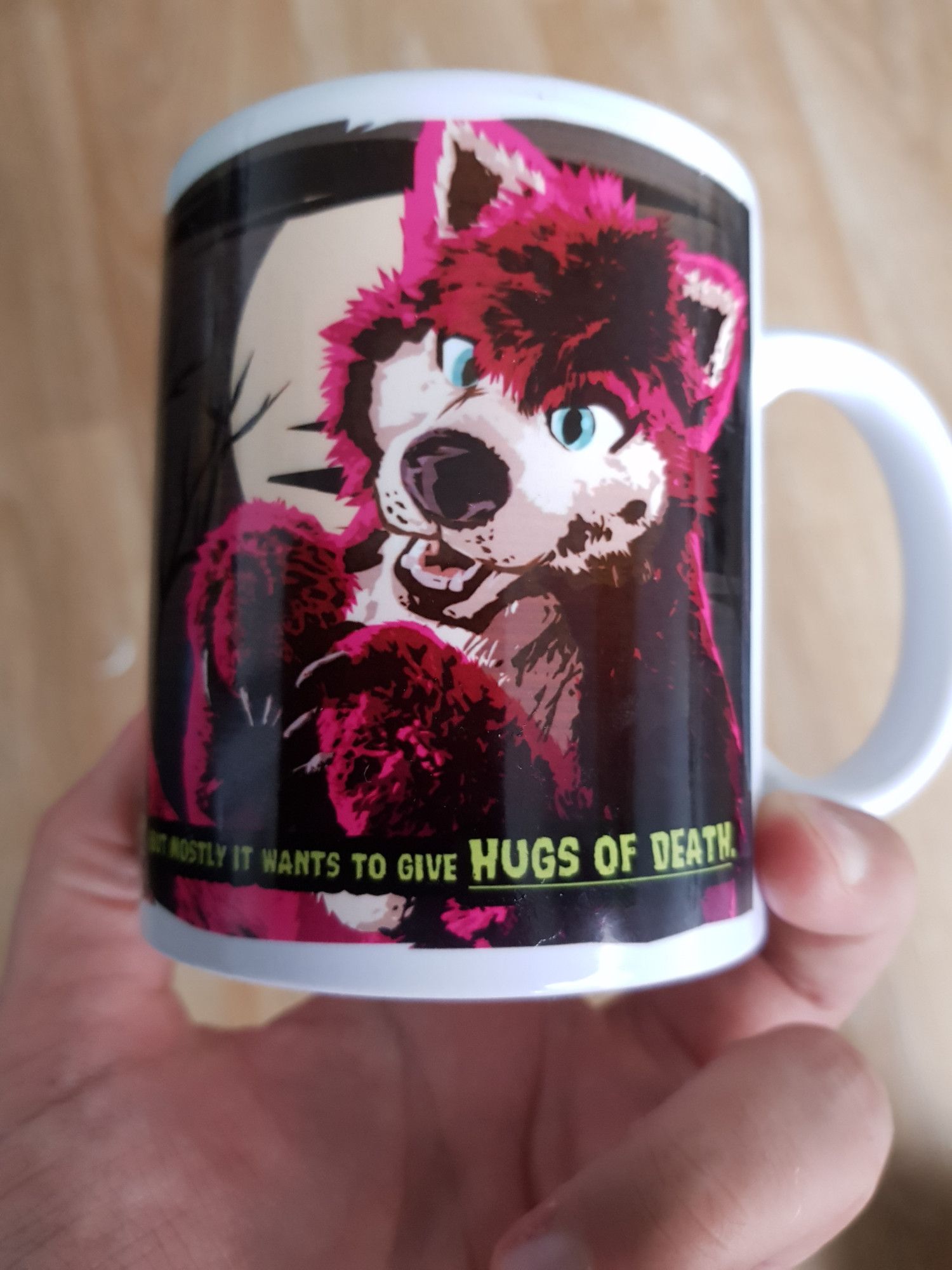 A mug with a pink wolf fursuit on it, miming a cutesy bark. The backdrop is a dark night with the full moon.
It reads: It's fluffy. But mostly it wants to give hugs of death.