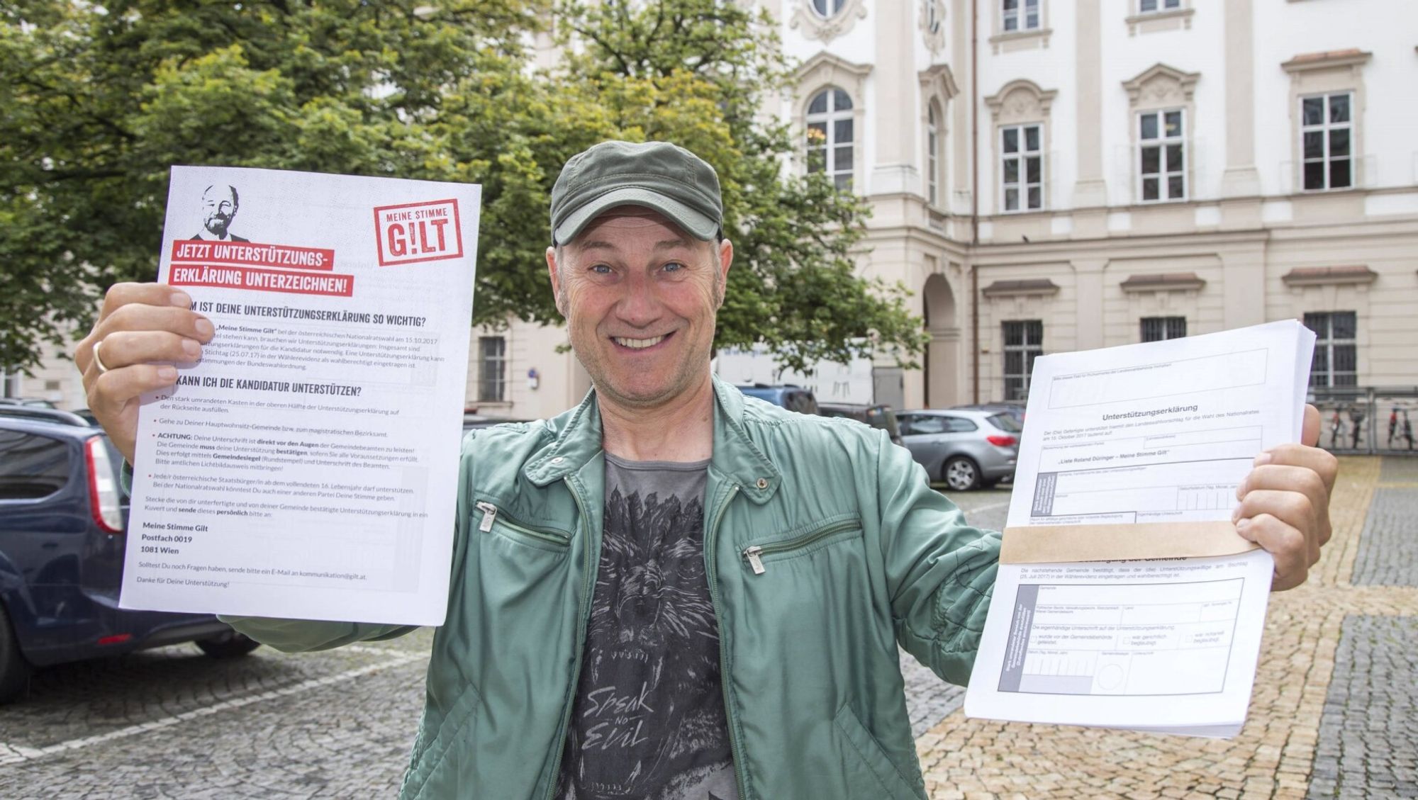 Roland Düringer präsentiert Unterschriften, die zum Antritt zur Nationalratswahl notwendig sind. Er hält die Zettel freudig mit beiden Händen in die Kamera. (2017)