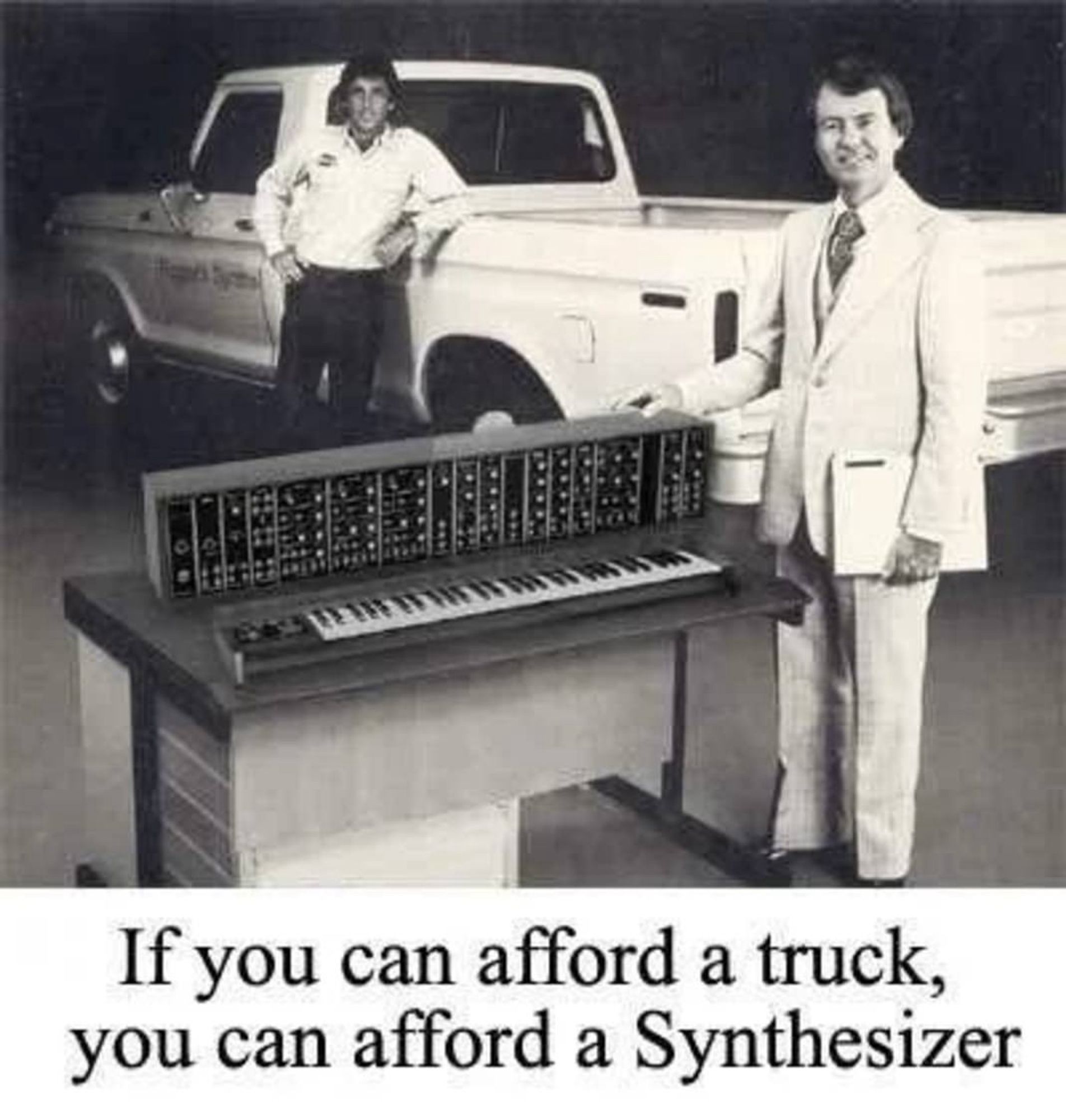 A black and white photo, one man in a white button up shirt tucked into dark pants leans on a light colored pickup that's parked facing away from the camera while another man closer to the camera stands to the right of a large synthesizer in a light colored full suit. At the bottom there is text that reads "If you can afford a truck, you can afford a Synthesizer"