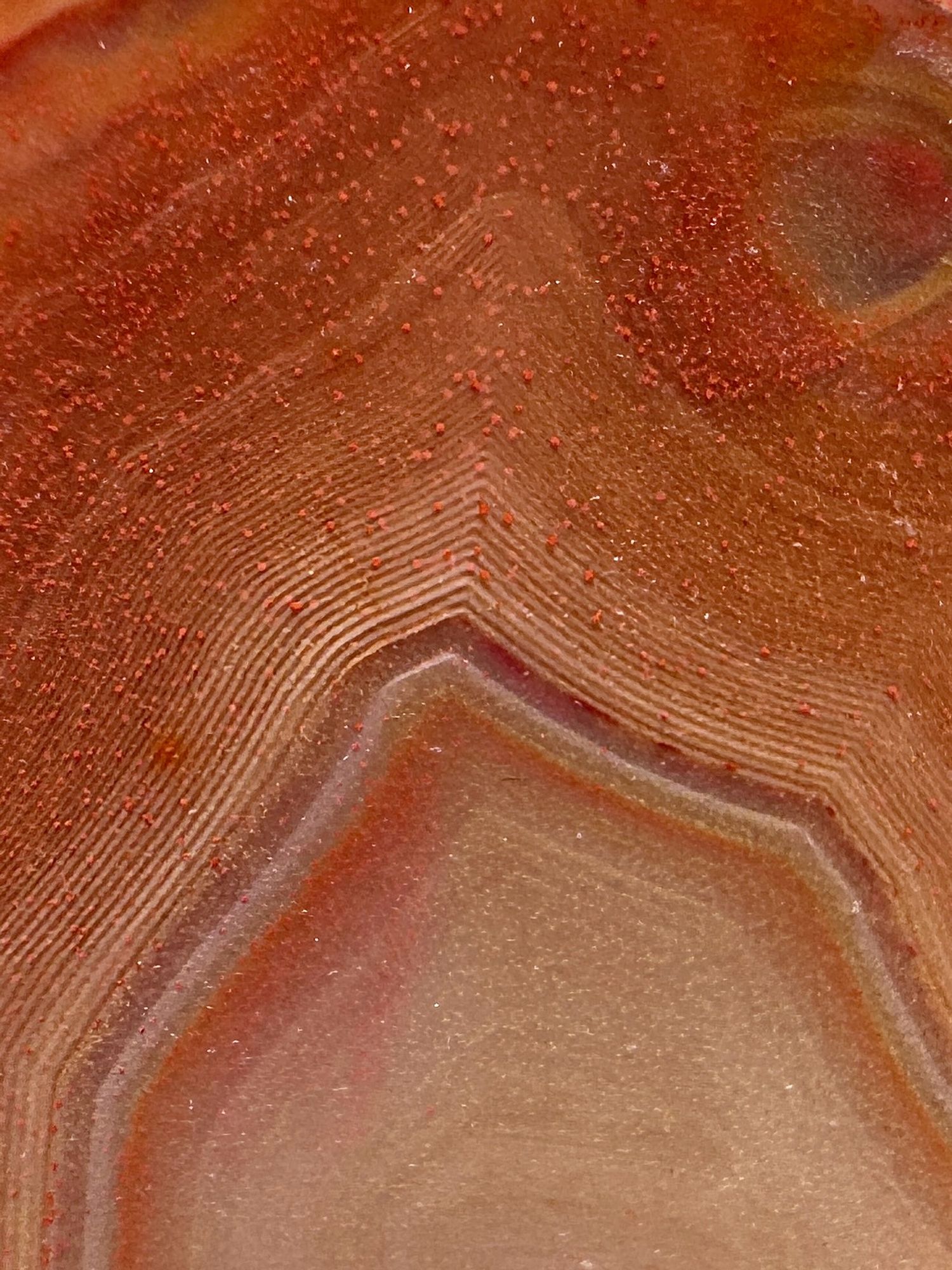 Photo showing a close up of the agate in the previous photo. The image shows an area of concentric angular banding forming a sharp point in the centre of the photo. The bands range in colour mostly through red to orange to white. Haematite remobilisation has resulted in red coloured staining and the presence of tiny wee red flecks of haematite throughout the agate.