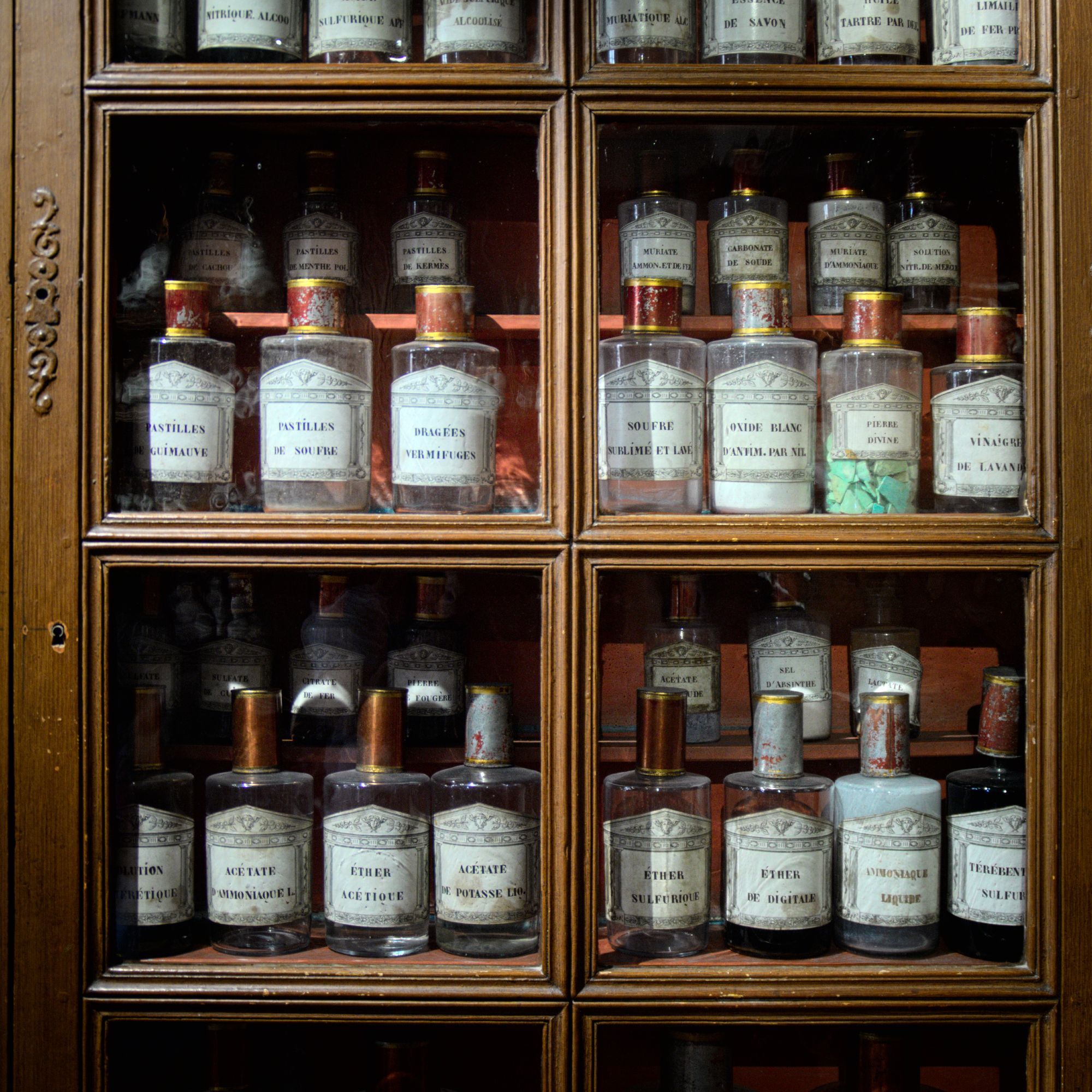 Une armoire vitrée de vieux produits pharmaceutiques dans des flacons en verre.