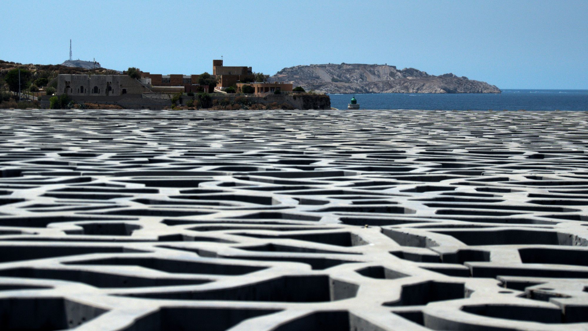 Le toit du MUCEM à Marseille photographié à raz. Au fond, on voit l'île du Frioul et un bout de mer.