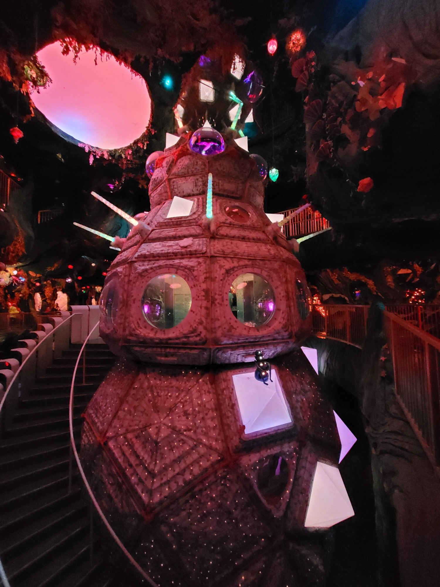 A 3 tiered structure with a staircase next to it in an alien forest. The structure has several glowing areas and portholes around the middle