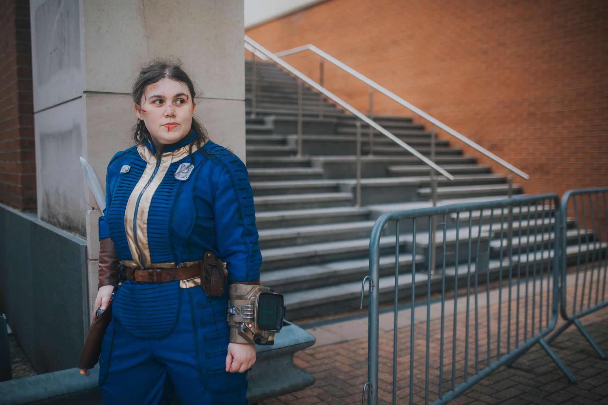 A photo of chloe dressed in a Fallout vault suit, in front of a set of stairs and a brick wall