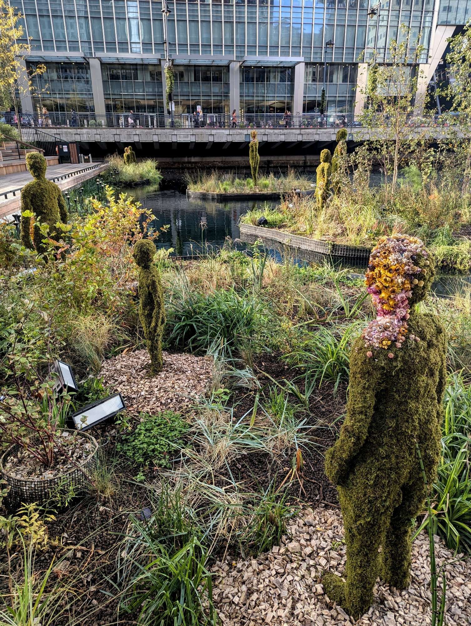 Human-shaped figures made of plants stand in patches of foliage.