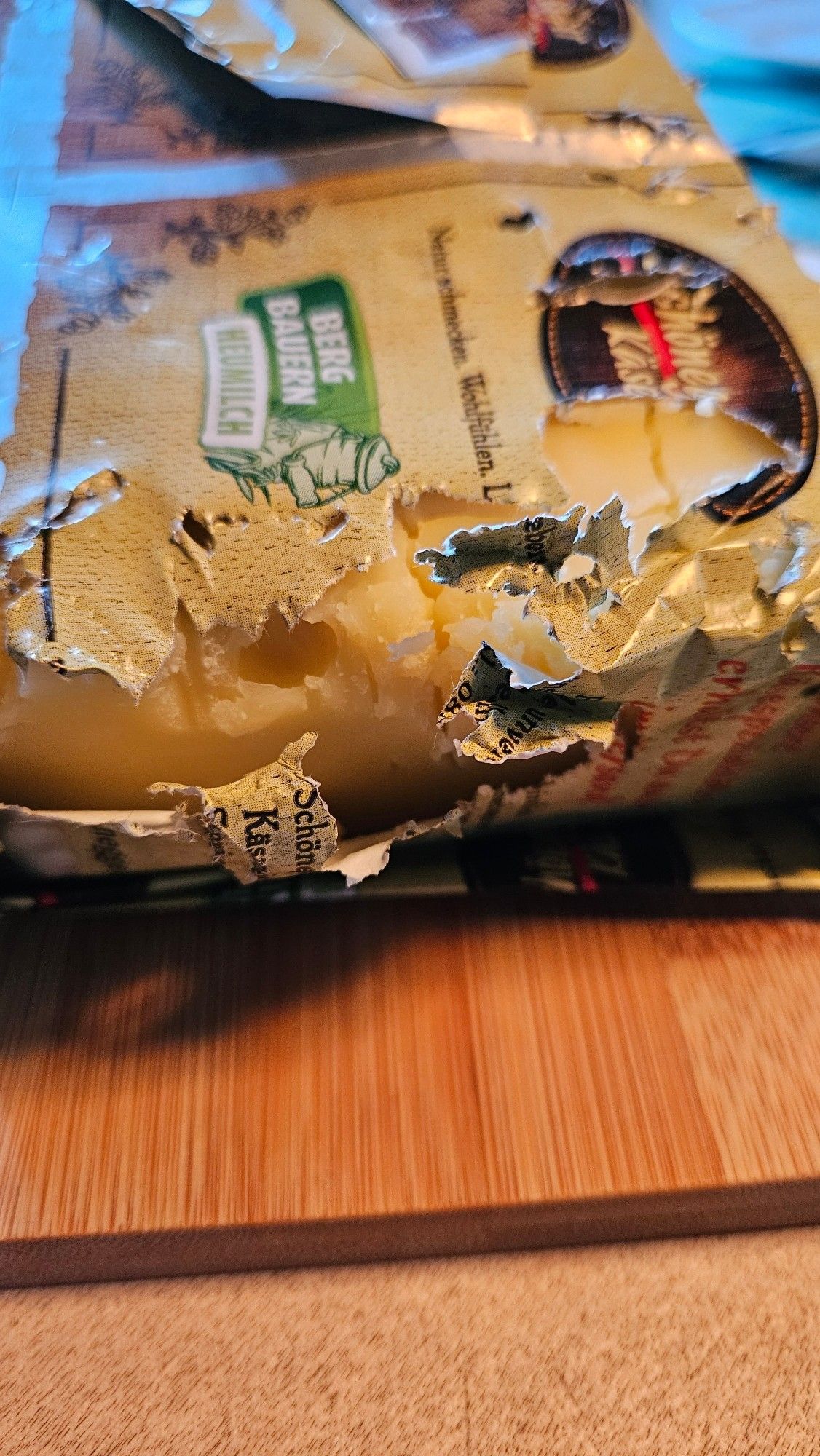 Eingepackter Käse. Die Verpackung ist teilweise aufgerissen und weist Bissspuren auf.