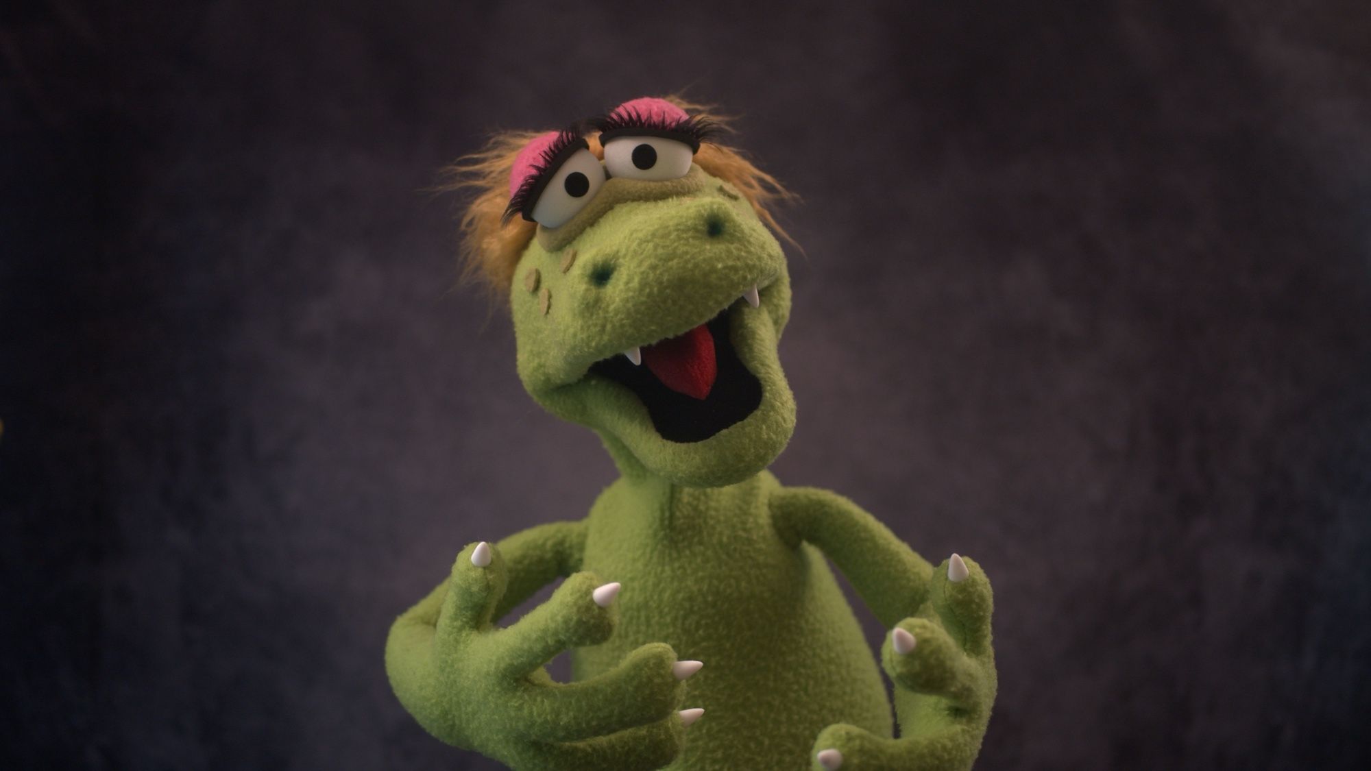 Front view of a green alligator puppet with blonde hair and large eyelashes