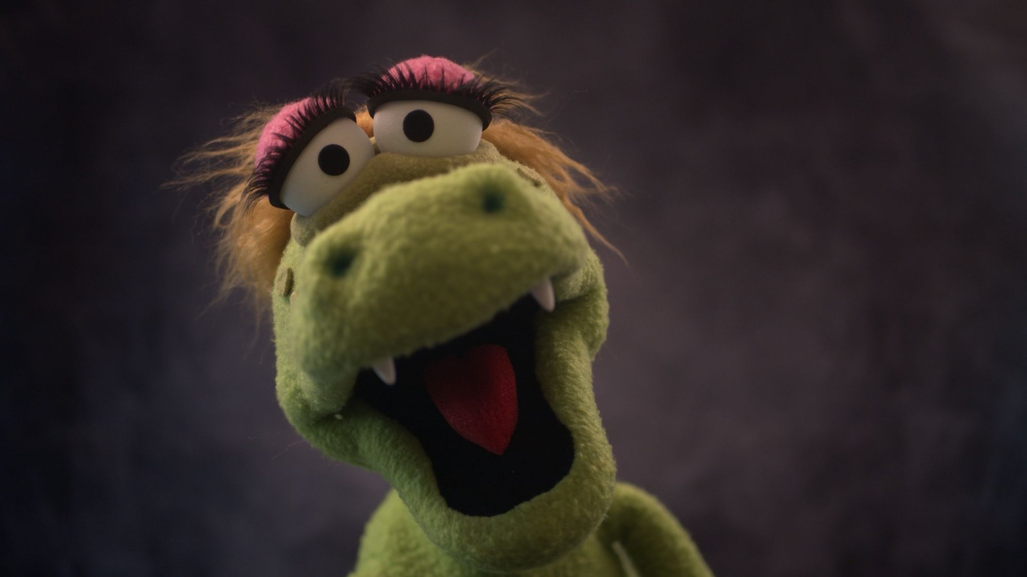 Closeup view of a green alligator puppet with blonde hair and large eyelashes