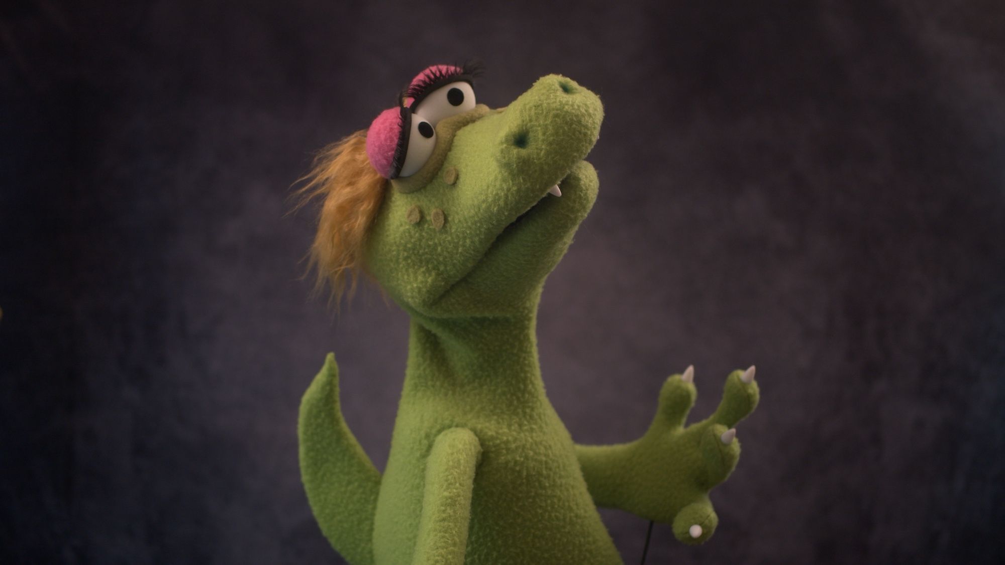 Left view of a green alligator puppet with blonde hair and large eyelashes