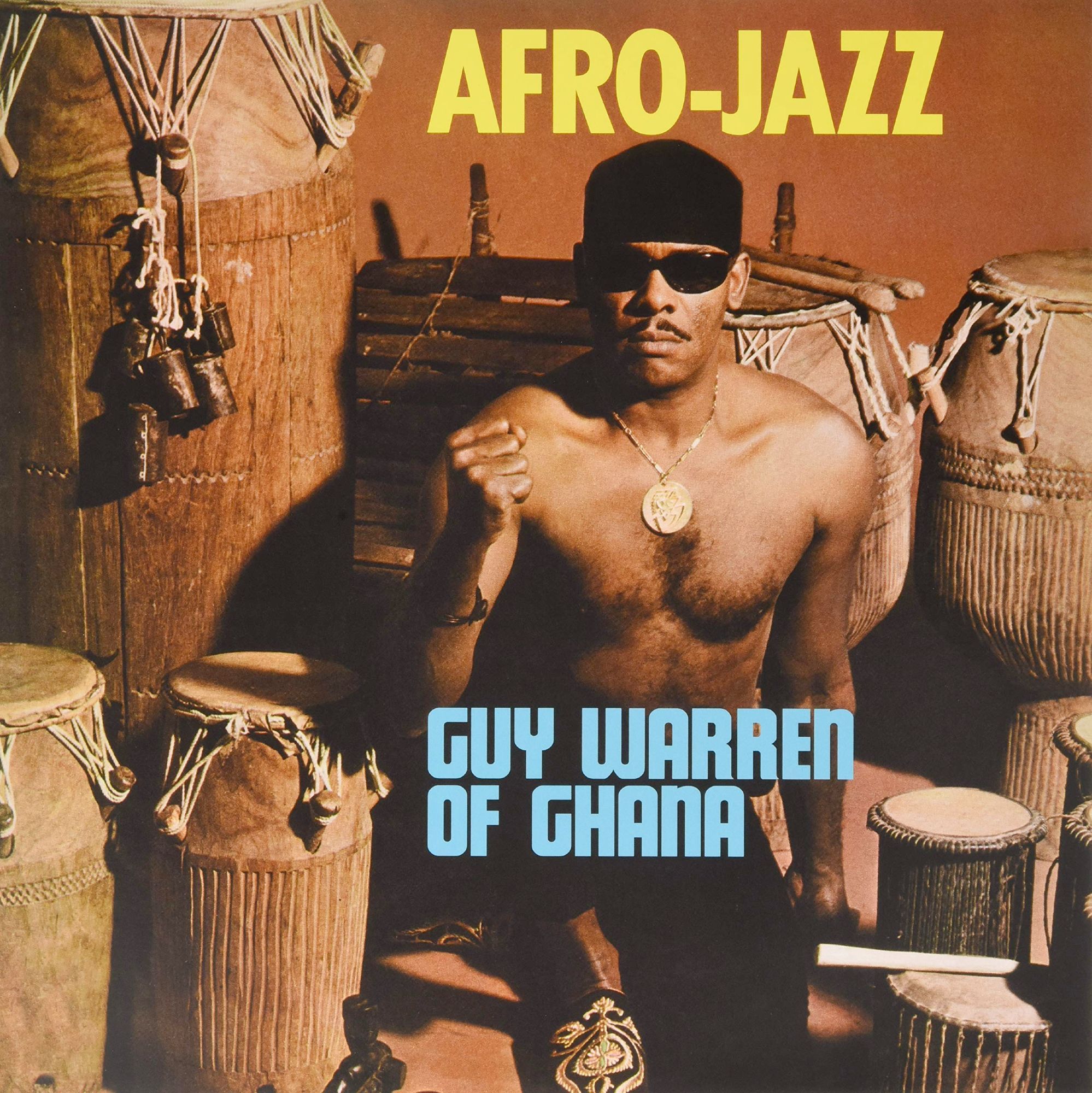 Album cover Afro-Jazz by Guy Warren, he is shirtless, wearing sunglasses, and raising his fist next to a bunch of drums