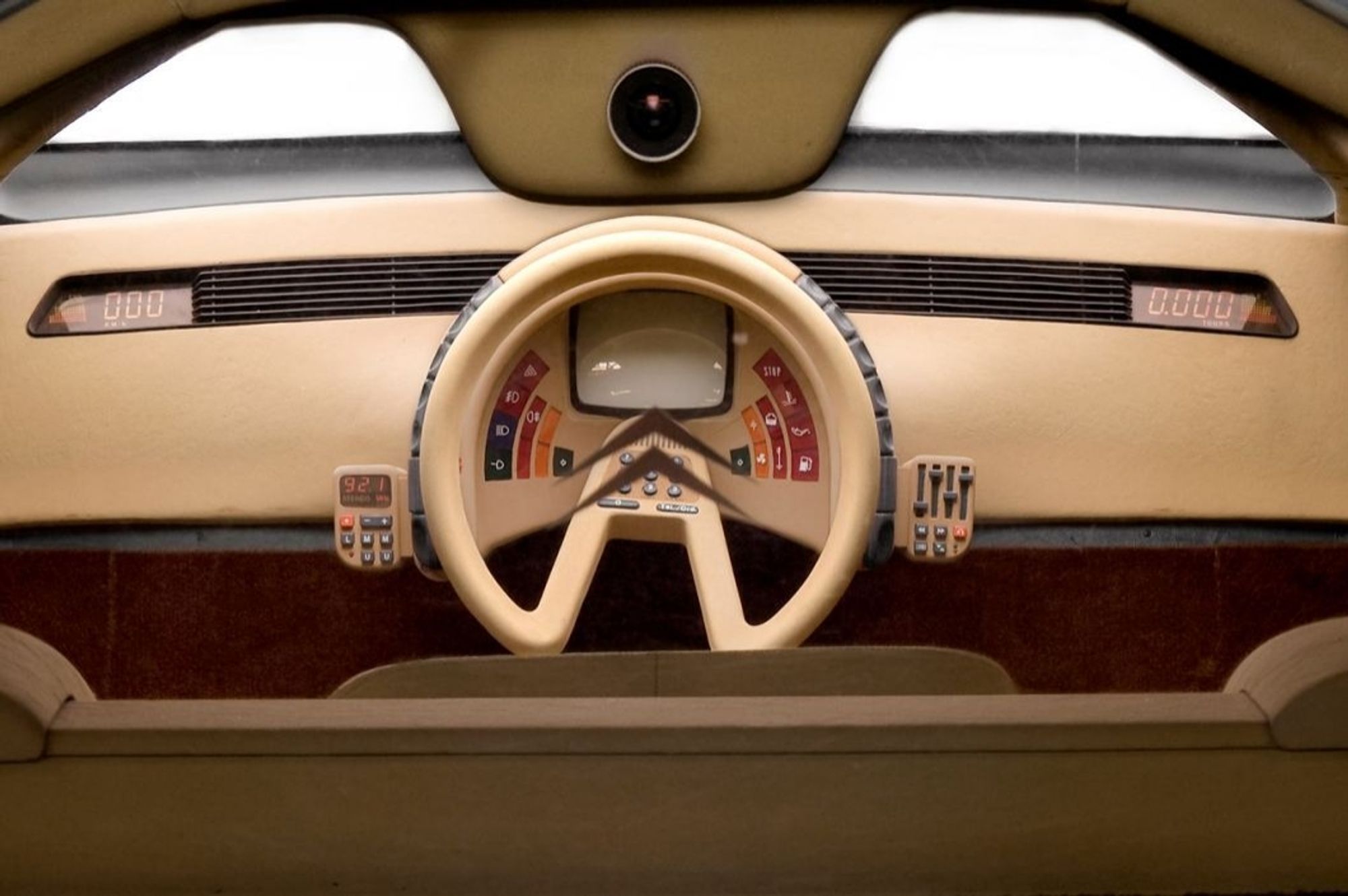 A head-on view of the steering wheel and dashboard with all kinds of fancy buttons and switches on it and even what looks to be a little video screen in the center