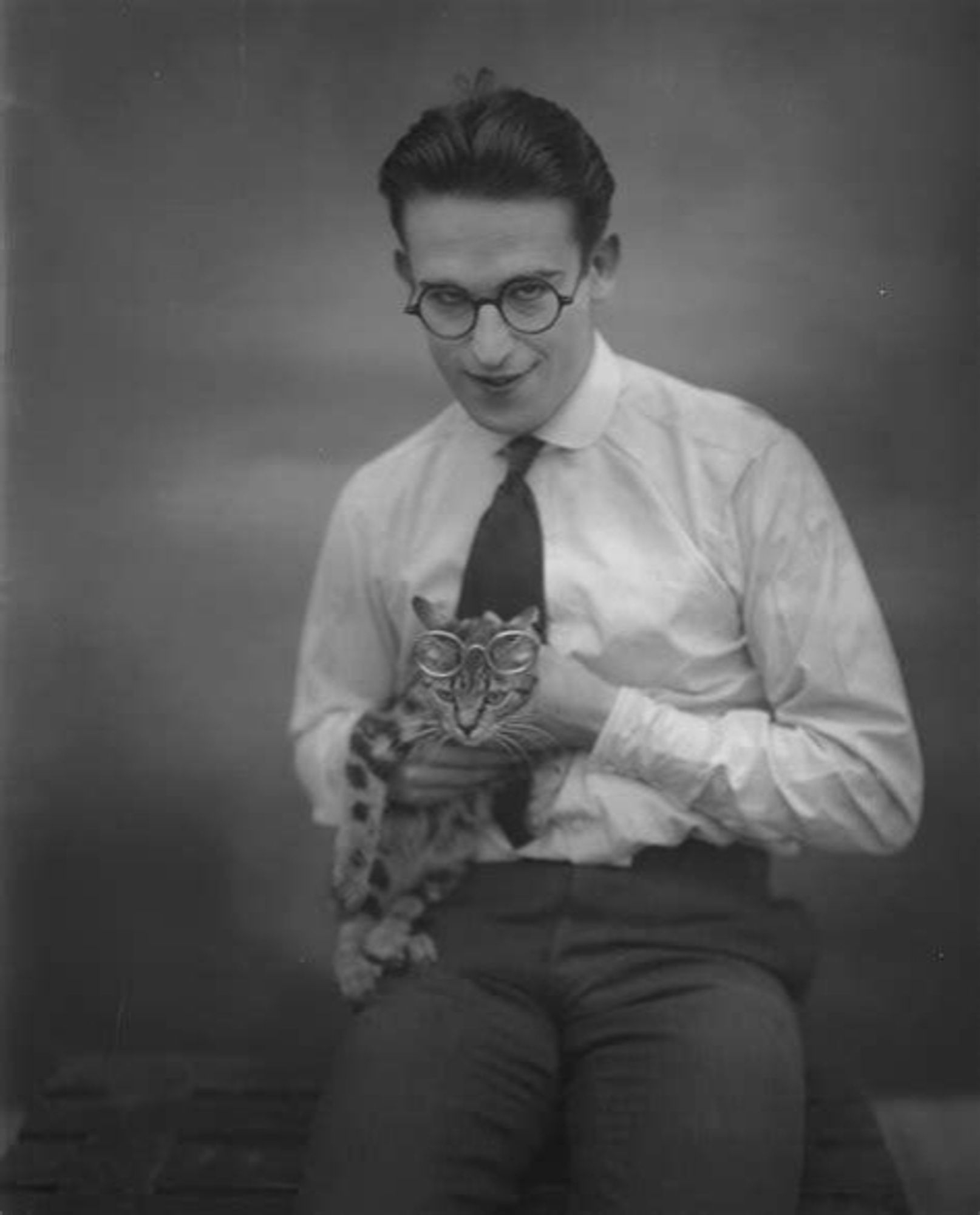 Black and white photograph of Harold Lloyd holding a cat they're both wearing glasses, although the cat's are pushed up on its forehead