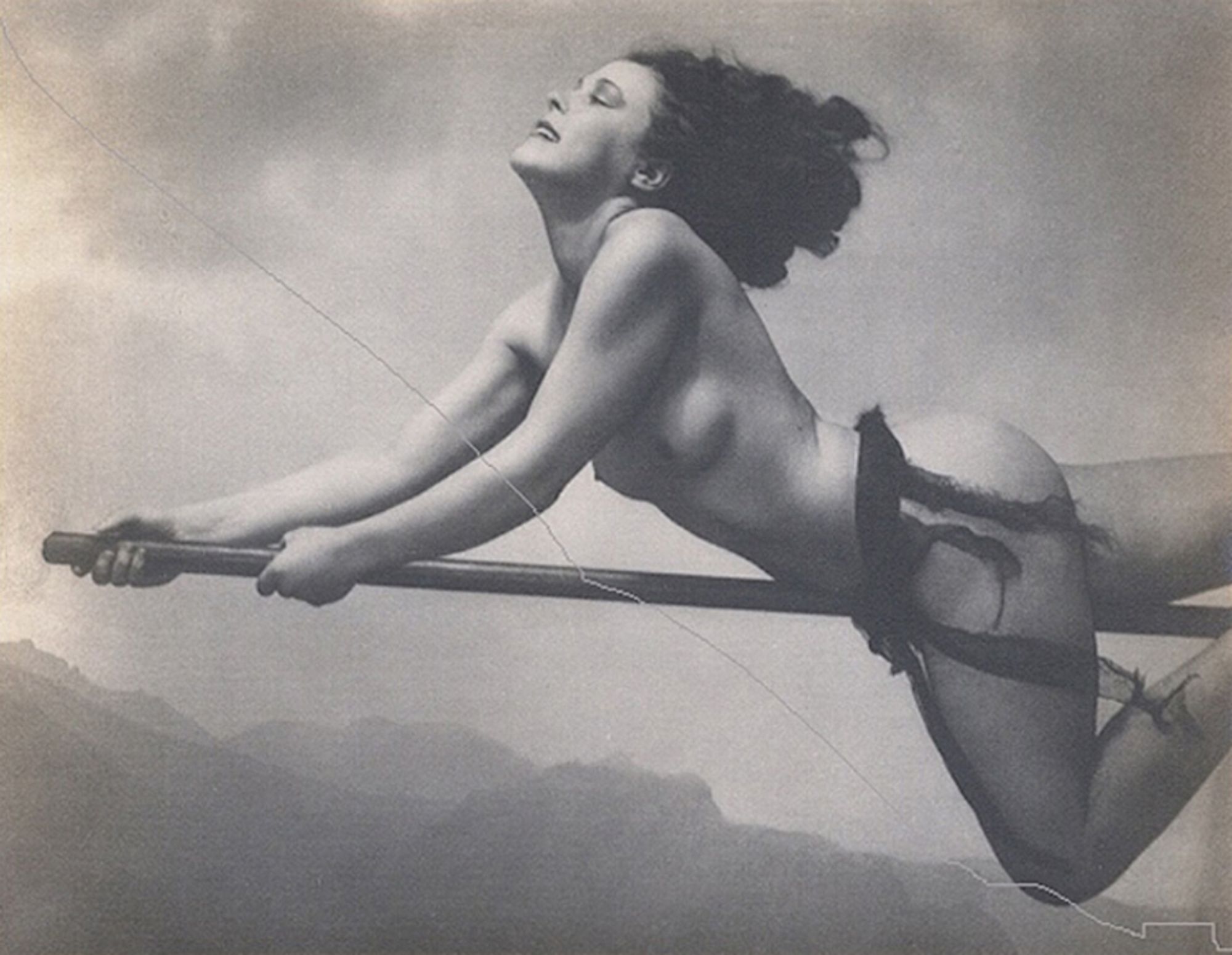 b&w photo of a woman riding a broomstick in front of a backdrop of clouds