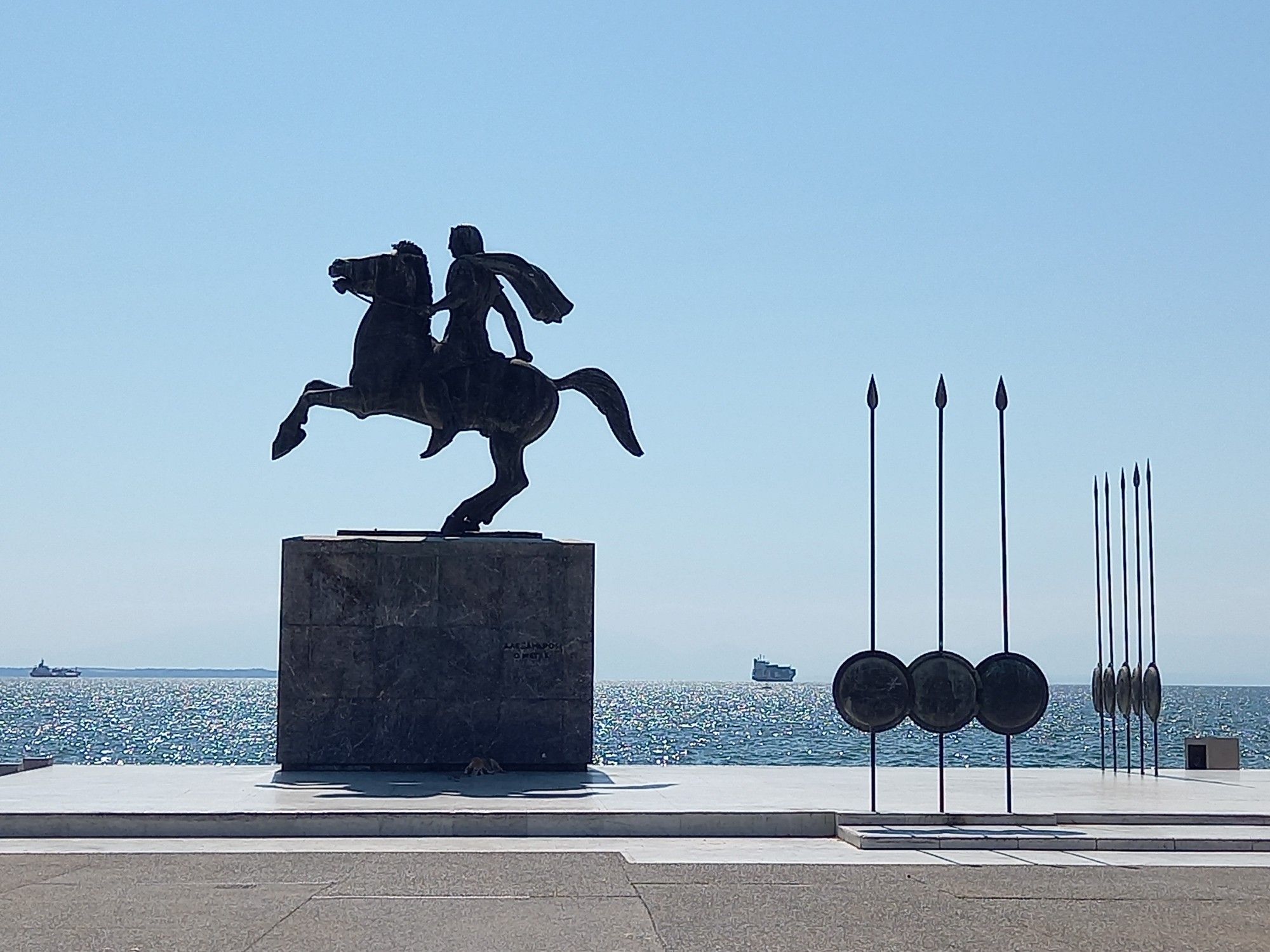 Statue of Alexander the Great on horseback, on top of a large base, by the seaside.