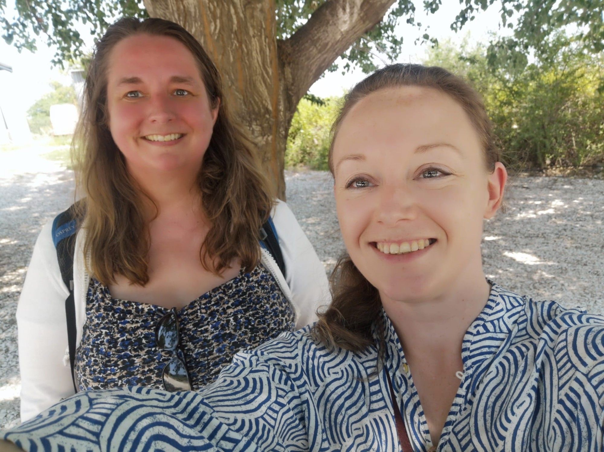 Two smiling individuals in the shade of a tree.