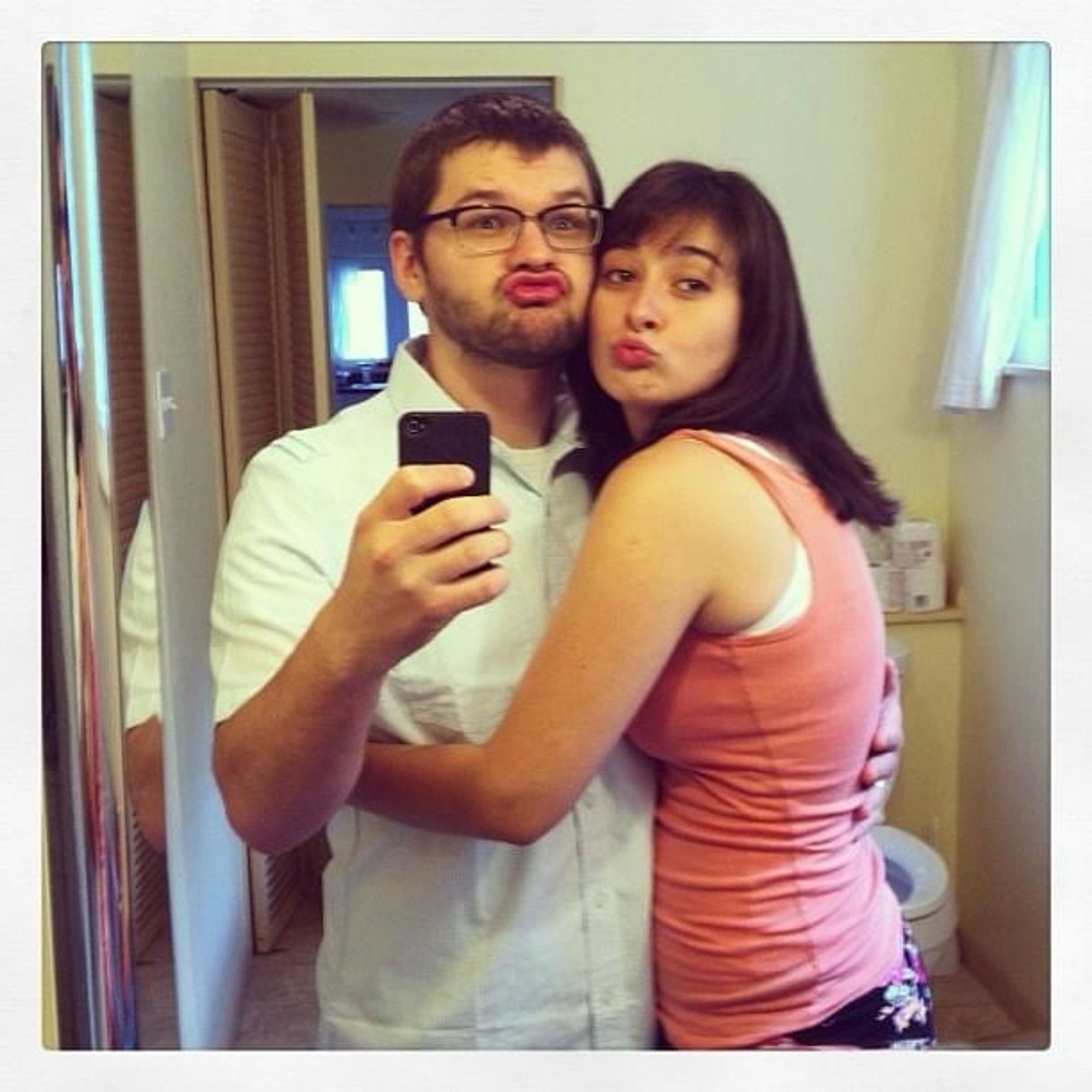 pre-transition willow with their ex-wife brittney taking a silly duck face kissy face selfie in a bathroom mirror c. august 2013. willow is insanely overdoing it and has an unstyled months overgrown buzzcut and a borderline-stubble beard and brittney has straightened, styled hair and light makeup. willow's short sleeve button-down still has crease marks in it. this photo is a real testament to the disparity between the couple's effort levels with regard to appearance, styling, and self-care in general