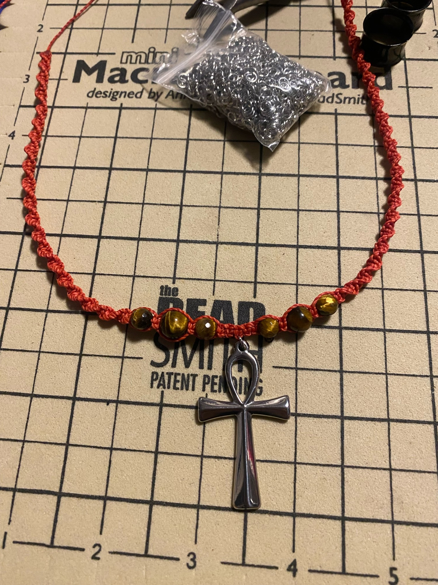 Silver ankh charm on a red macrame choker with tigers eye beads.