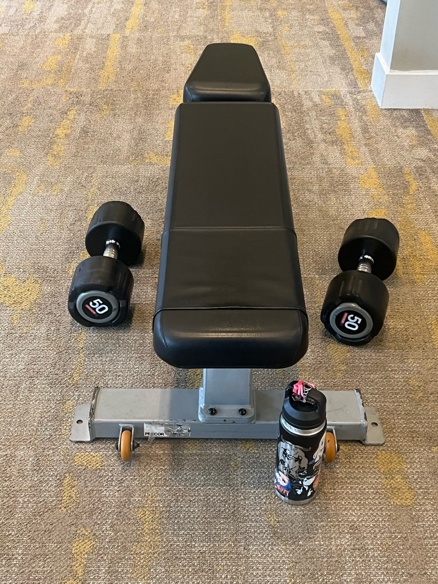 an irvine company apartment gym weight bench with some 50 pound dumbbells for pressing and my wow team water bottle covered in stickers