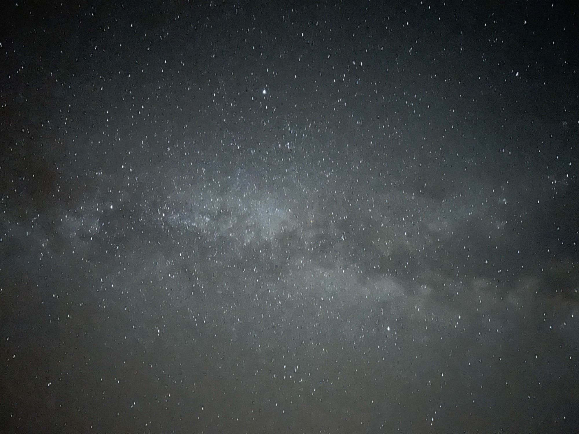 A sky full of stars. A brighter band with a dark rift runs horizontally across the middle. It is our galaxy in the general direction of the Summer Triangle (Deneb is left-middle, Vega is top-middle, and Altair is lower-right); the rift is the Northern Coalsack, a dark cloud of dust blocking the stars beyond it.