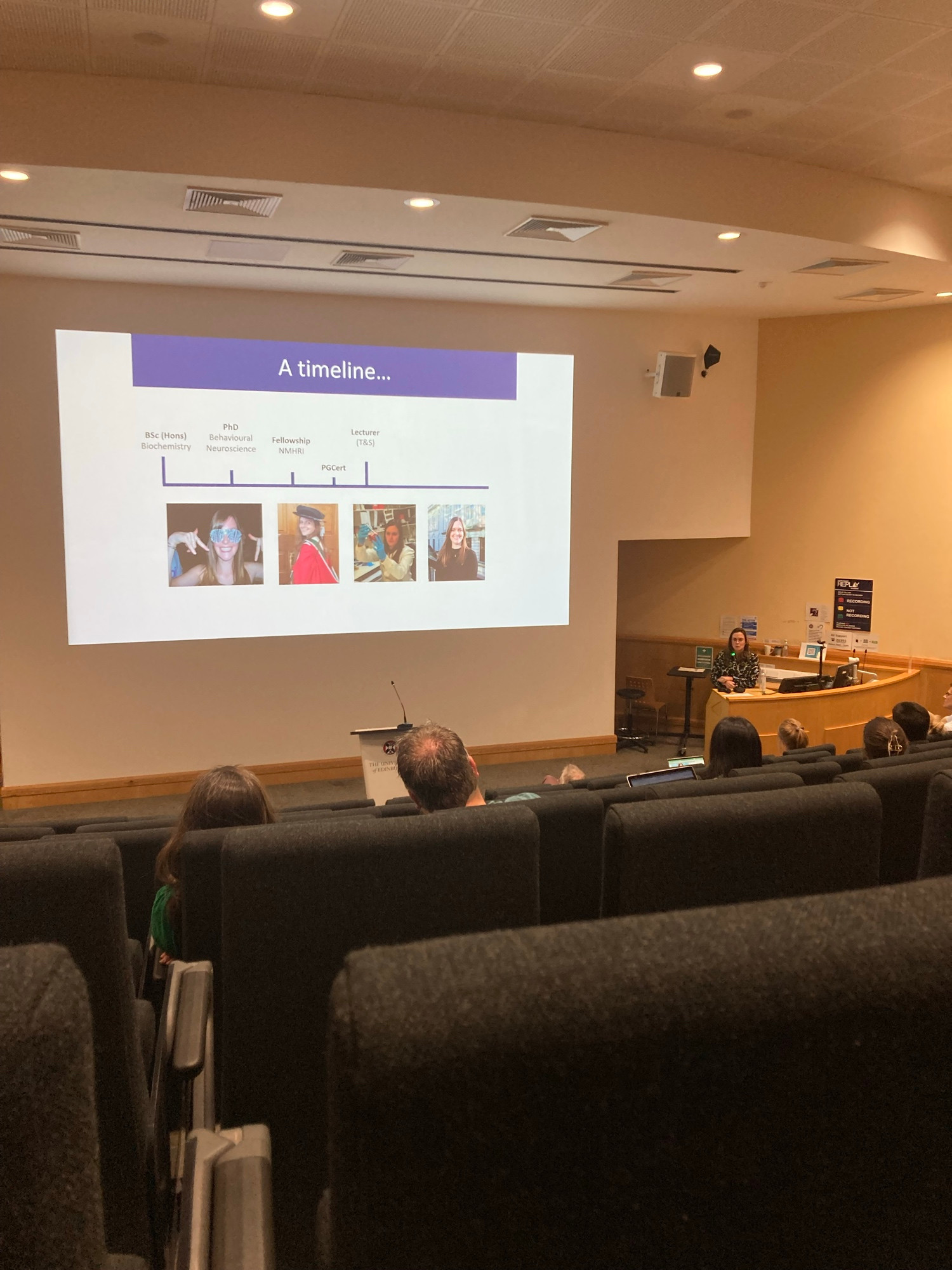 A lecture theatre with a slide that says a timeline…. Showing a small overview of Emma’s career whilst she talks about it. 